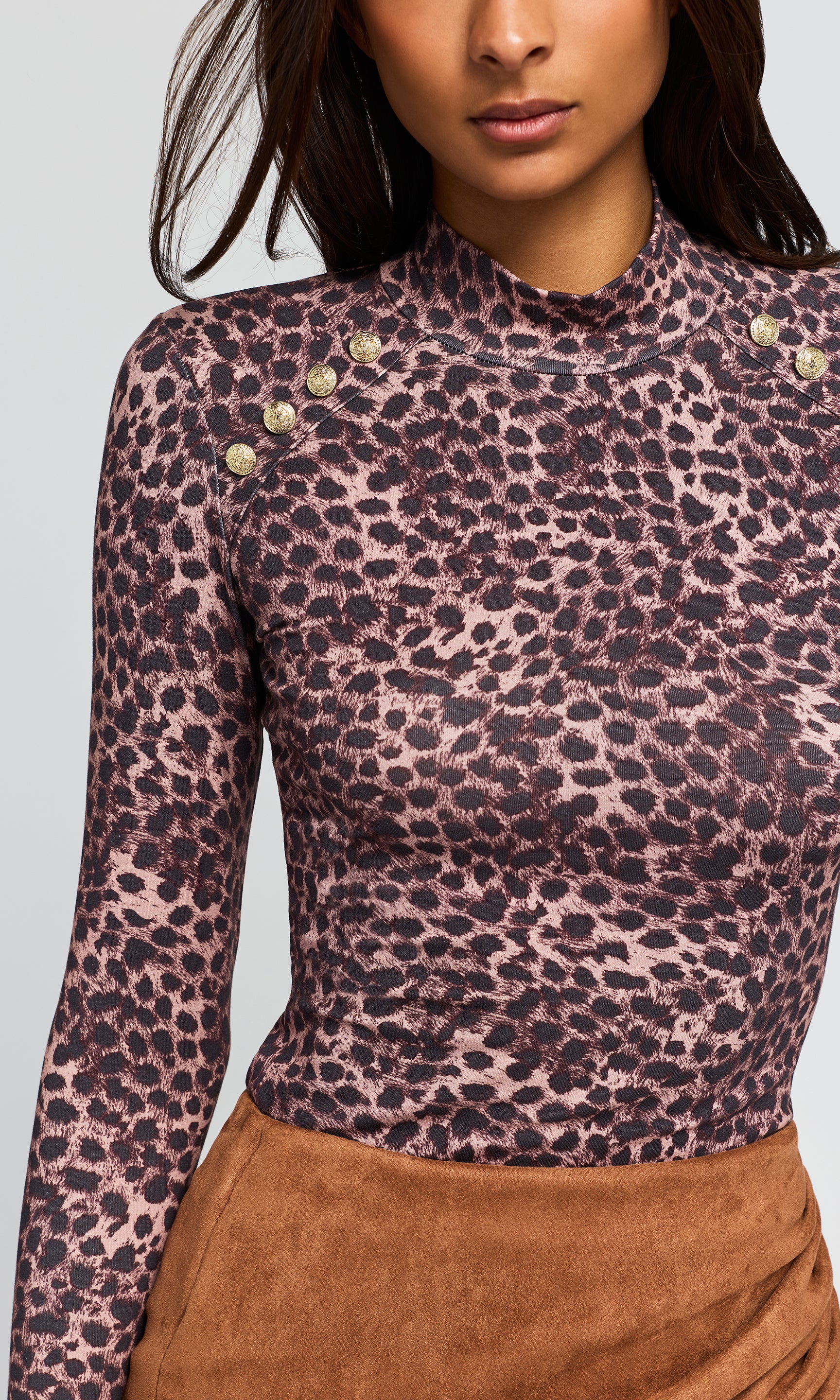 Close-up of a long-sleeve mock neck top with a brown leopard print and gold-tone shoulder buttons, paired with a brown skirt.