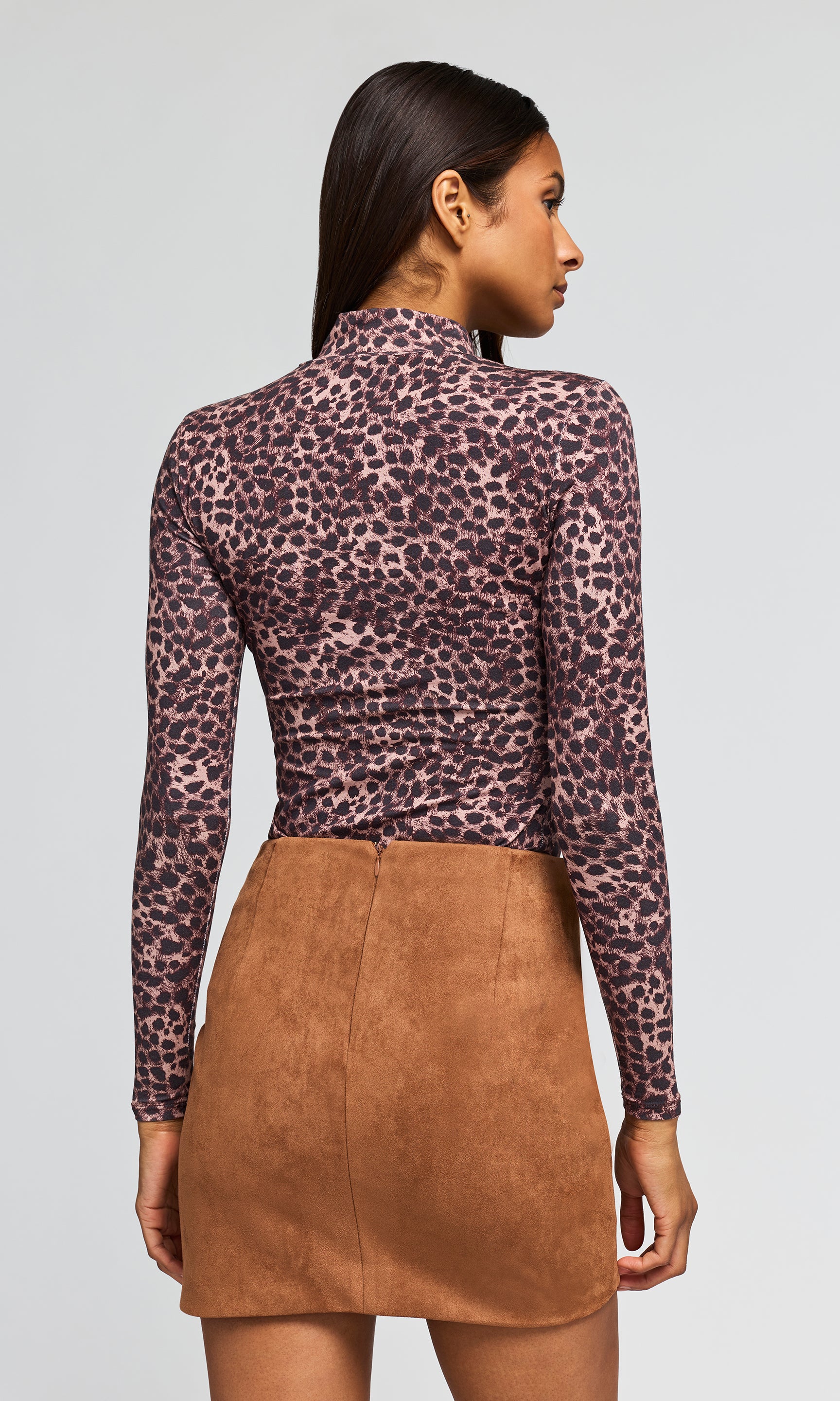 Back view of model wearing a long-sleeve leopard-print top with gold button details on the shoulders and a brown faux-suede mini skirt.