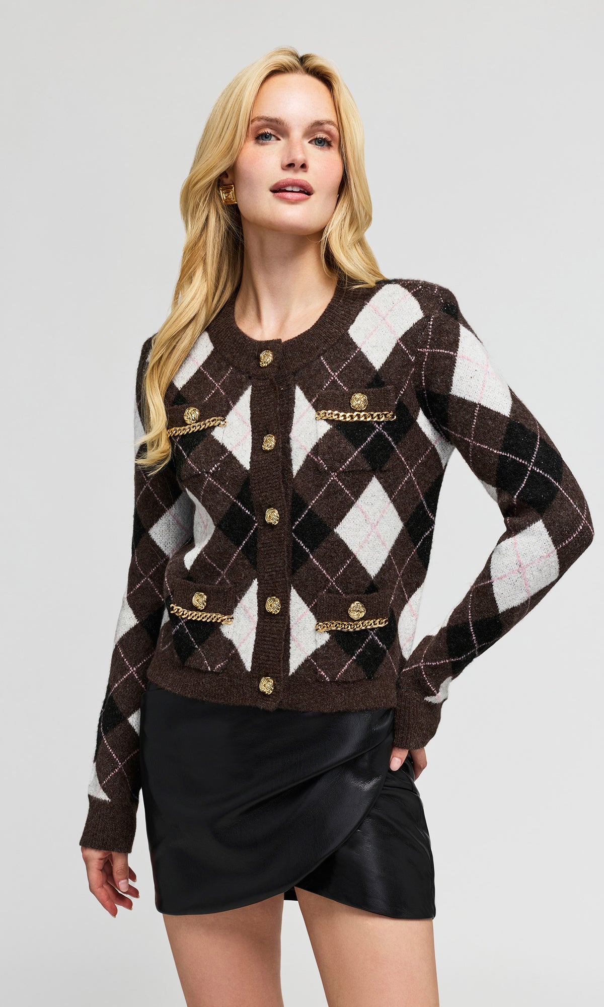 Model wearing a cropped brown argyle cardigan with gold-tone buttons and chain details, paired with a black mini skirt.