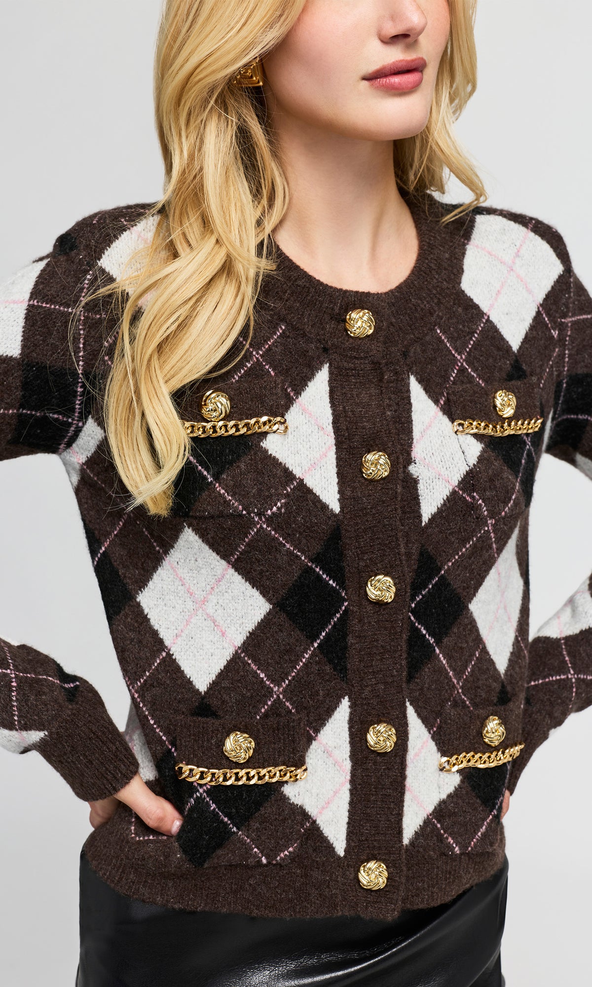 Close-up of a woman wearing a brown, black, and white argyle cardigan with gold buttons and chain trim pockets.