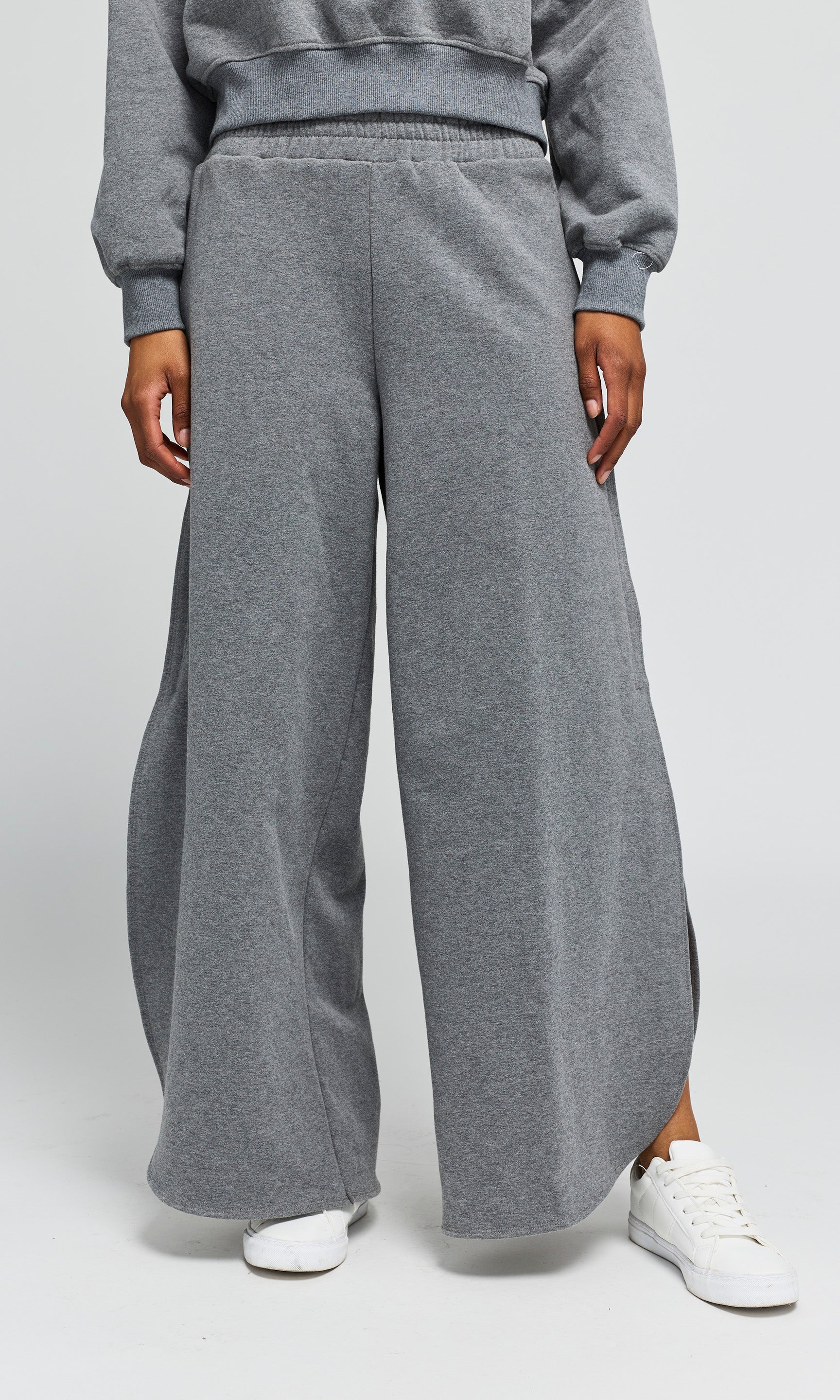 Person wearing a gray sweatshirt and wide-leg pants on a white background