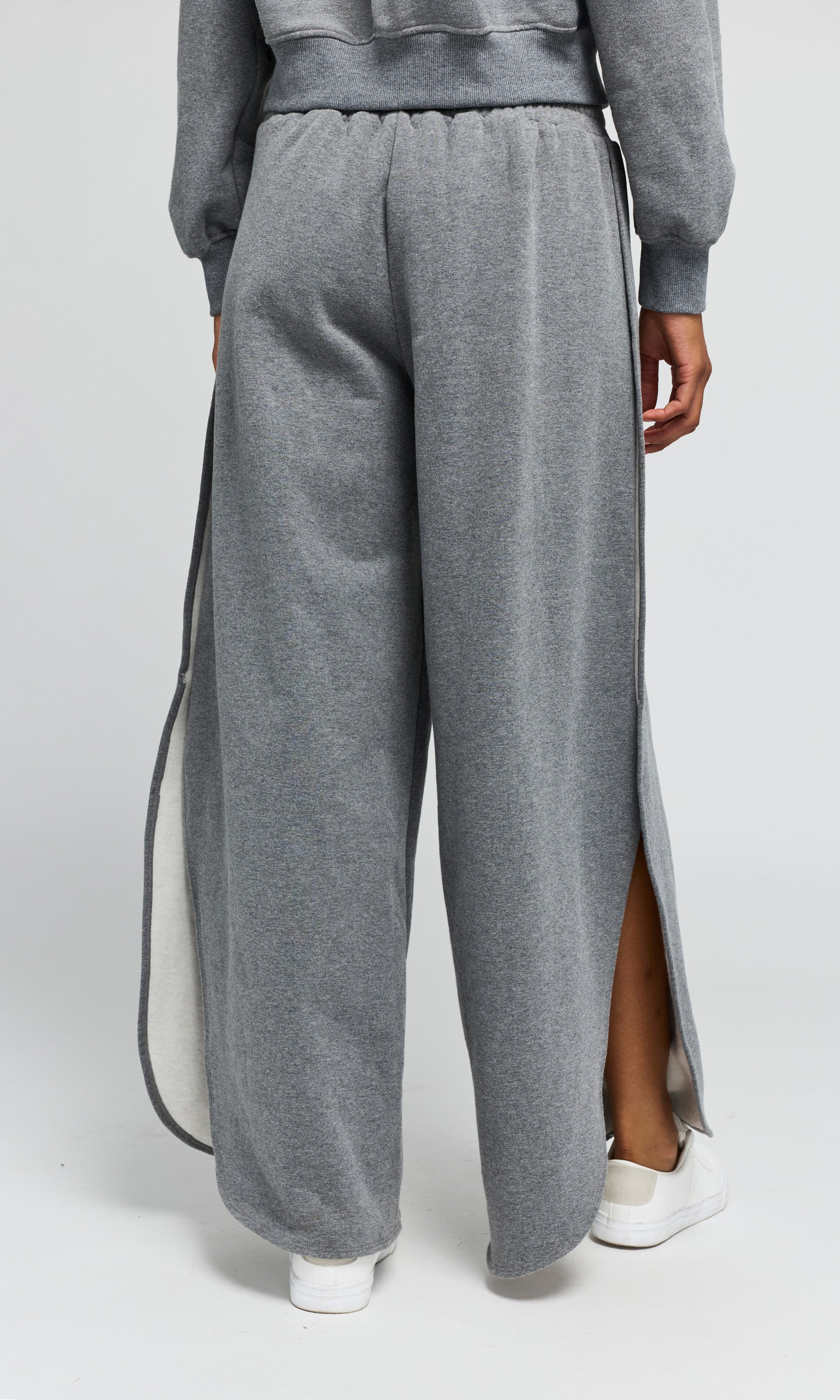 Back view of person wearing gray sweatpants with a side slit on a white background