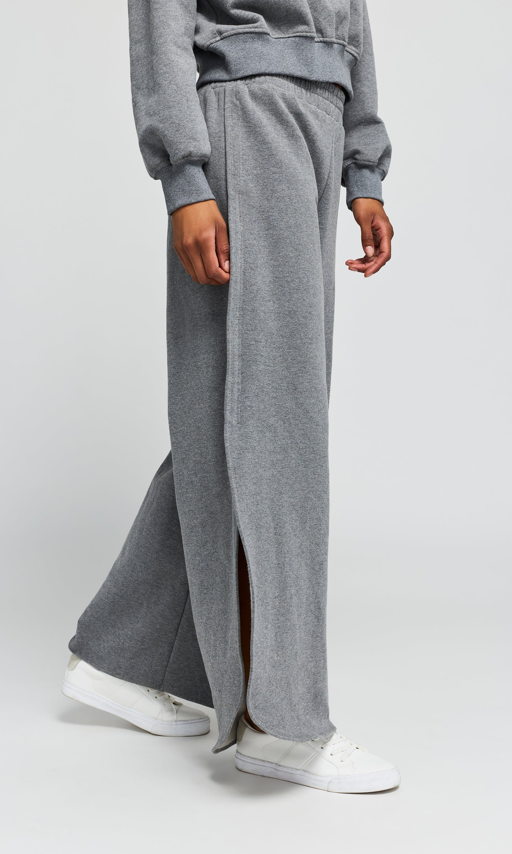 Side view of person wearing gray sweatpants with a front split on a white background