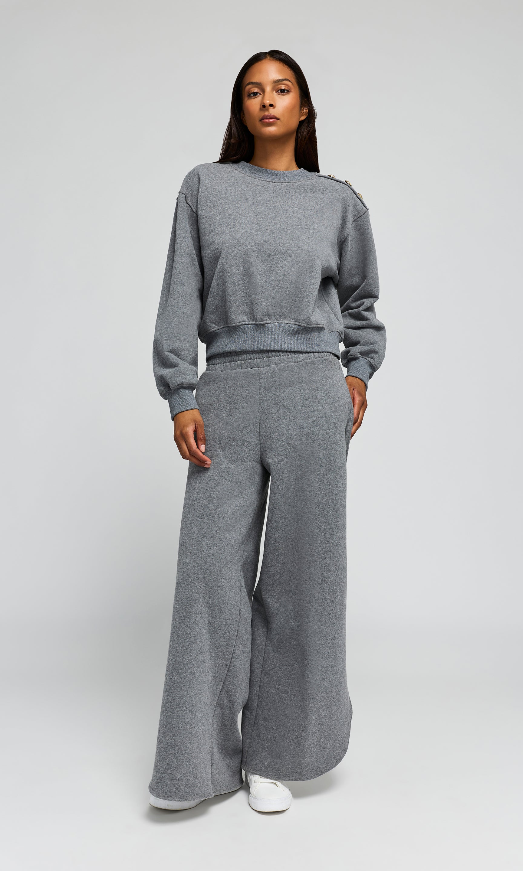 Woman wearing a gray sweatshirt and wide-leg pants on a white background