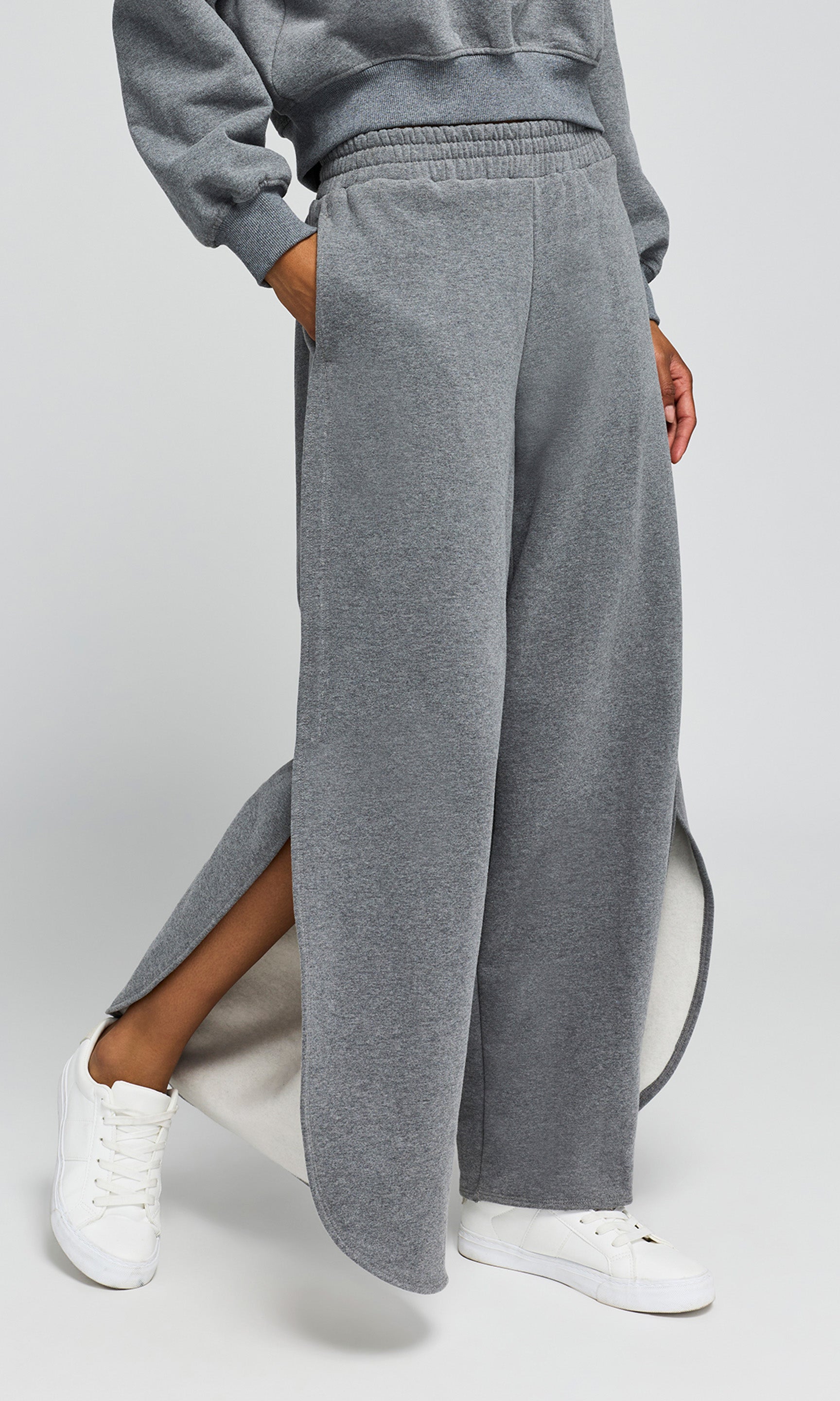 Side view of person wearing a gray tracksuit with wide-leg pants on a white background