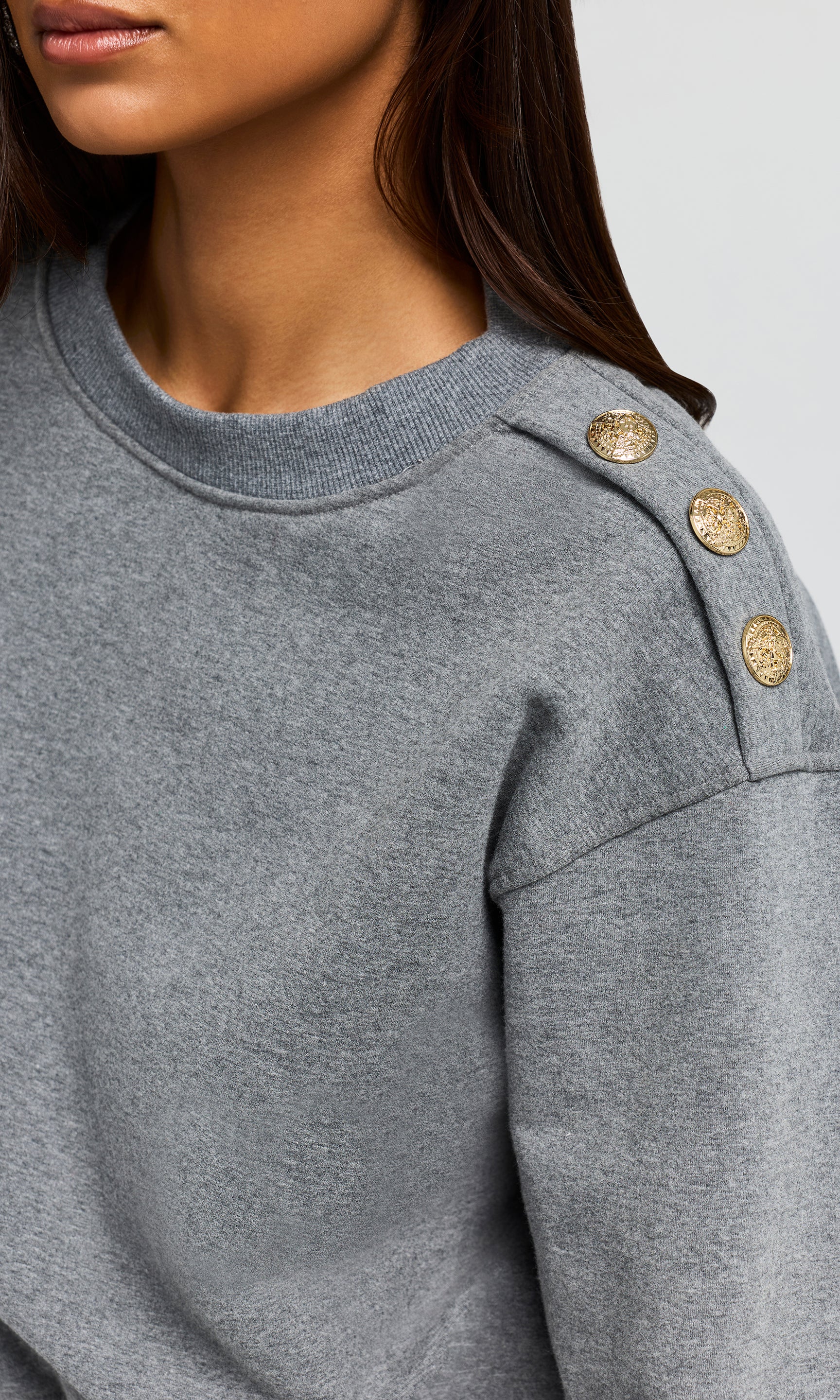 Close-up of gray sweater with gold buttons on a neutral background