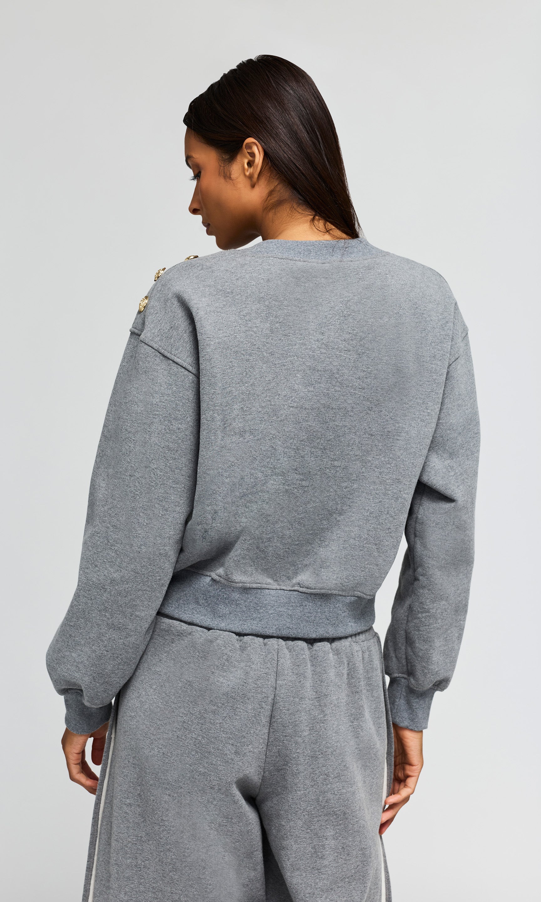 Back view of person wearing a gray sweatshirt and pants on a light gray background