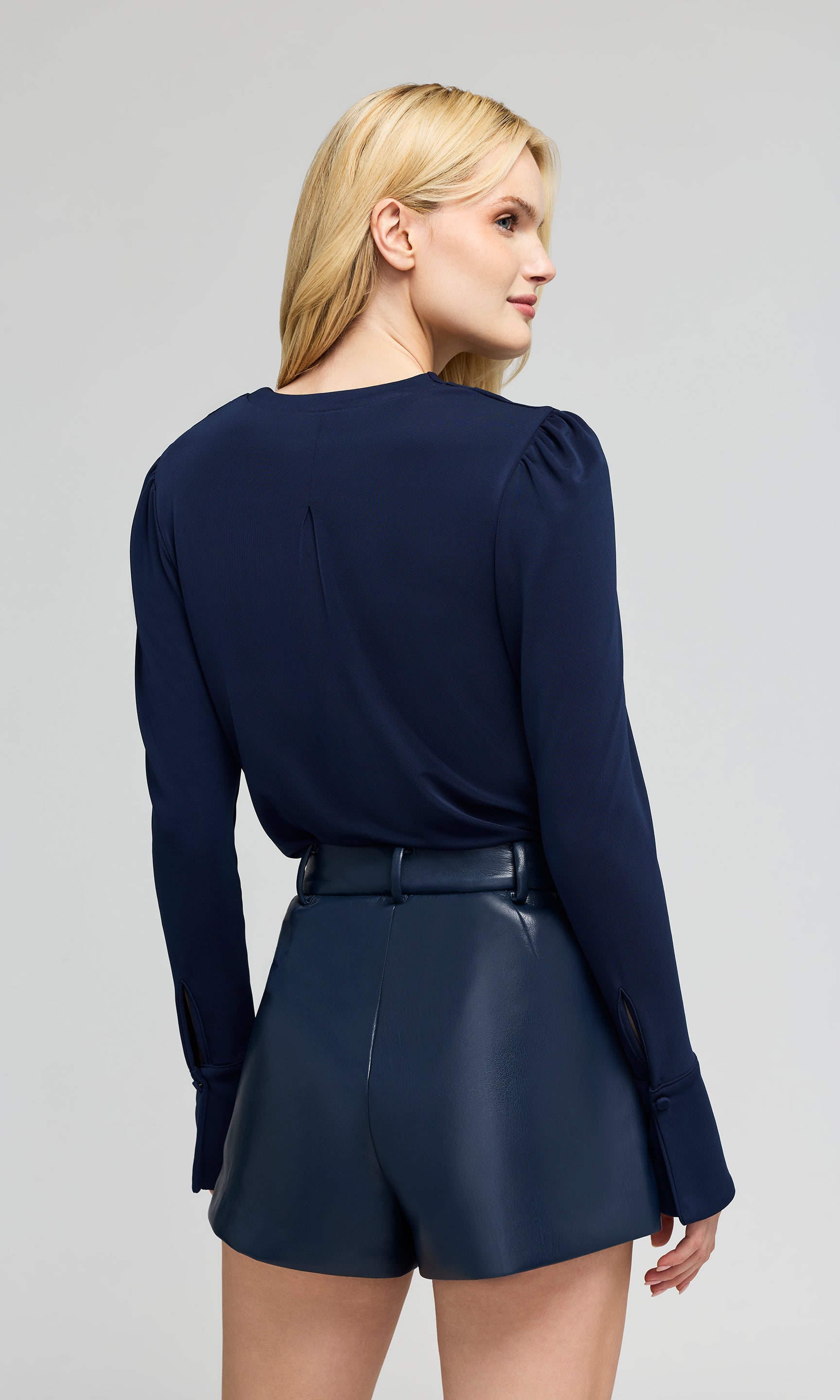 Back view of woman wearing a navy blue long-sleeve top and matching shorts on a gray background