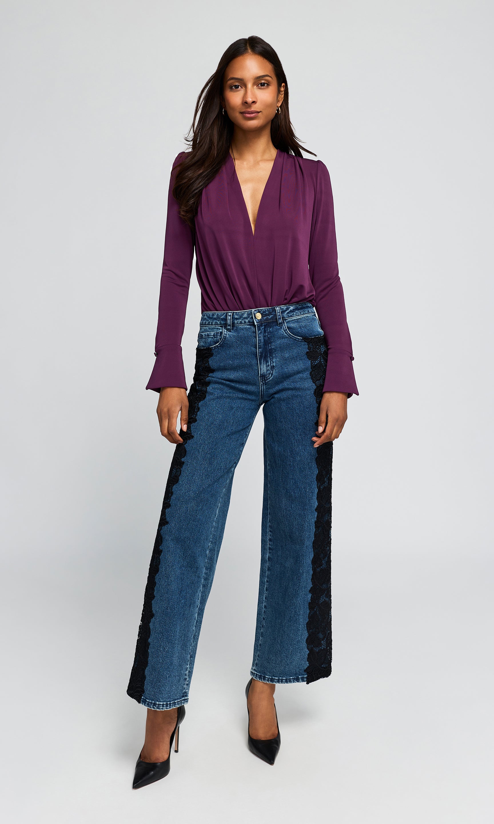 Model wearing a purple wrap-style blouse and high-waisted blue wide-leg jeans with black lace side panels, paired with black pointed heels.