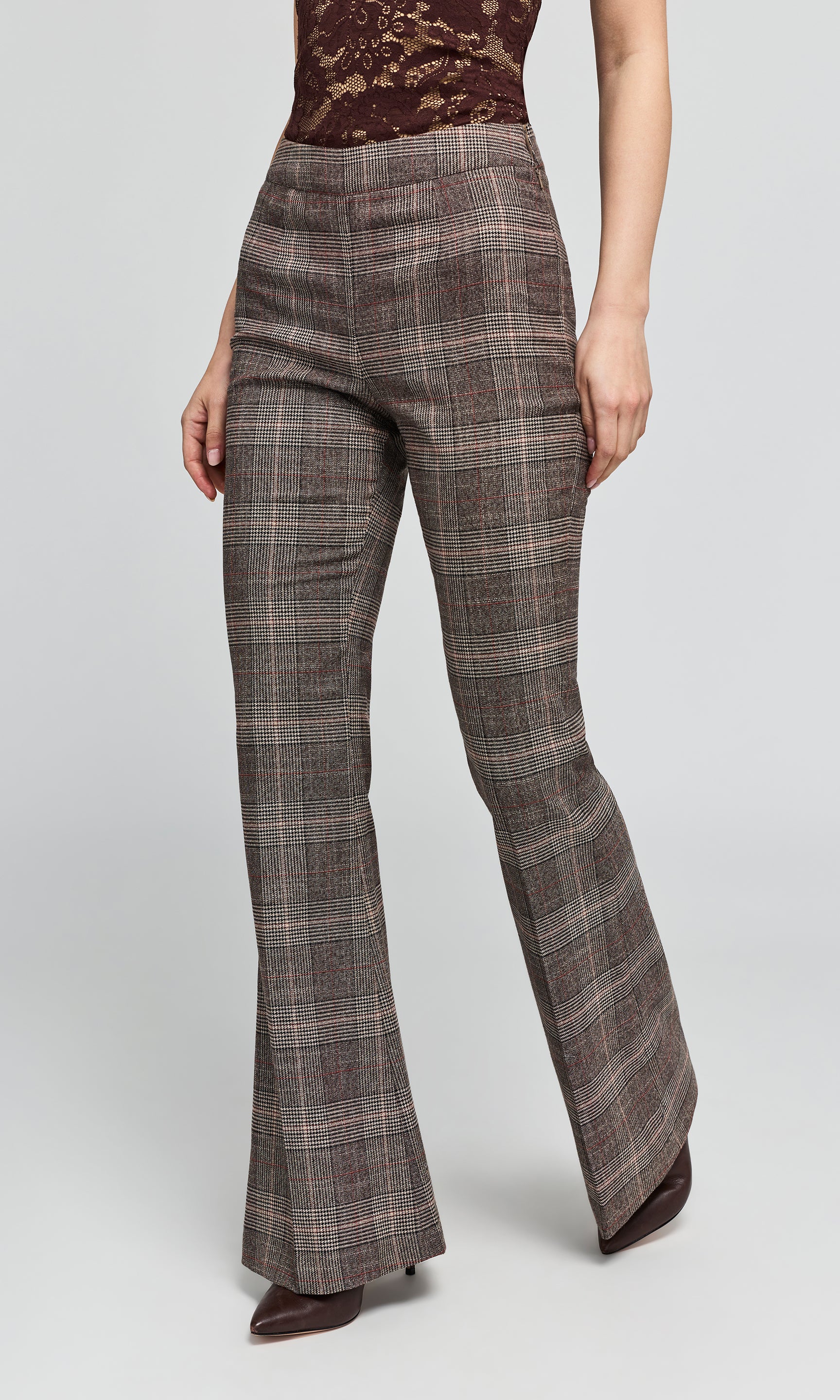Side view of model wearing a pair of brown and gray plaid flare pants with a lace top, on a plain background.