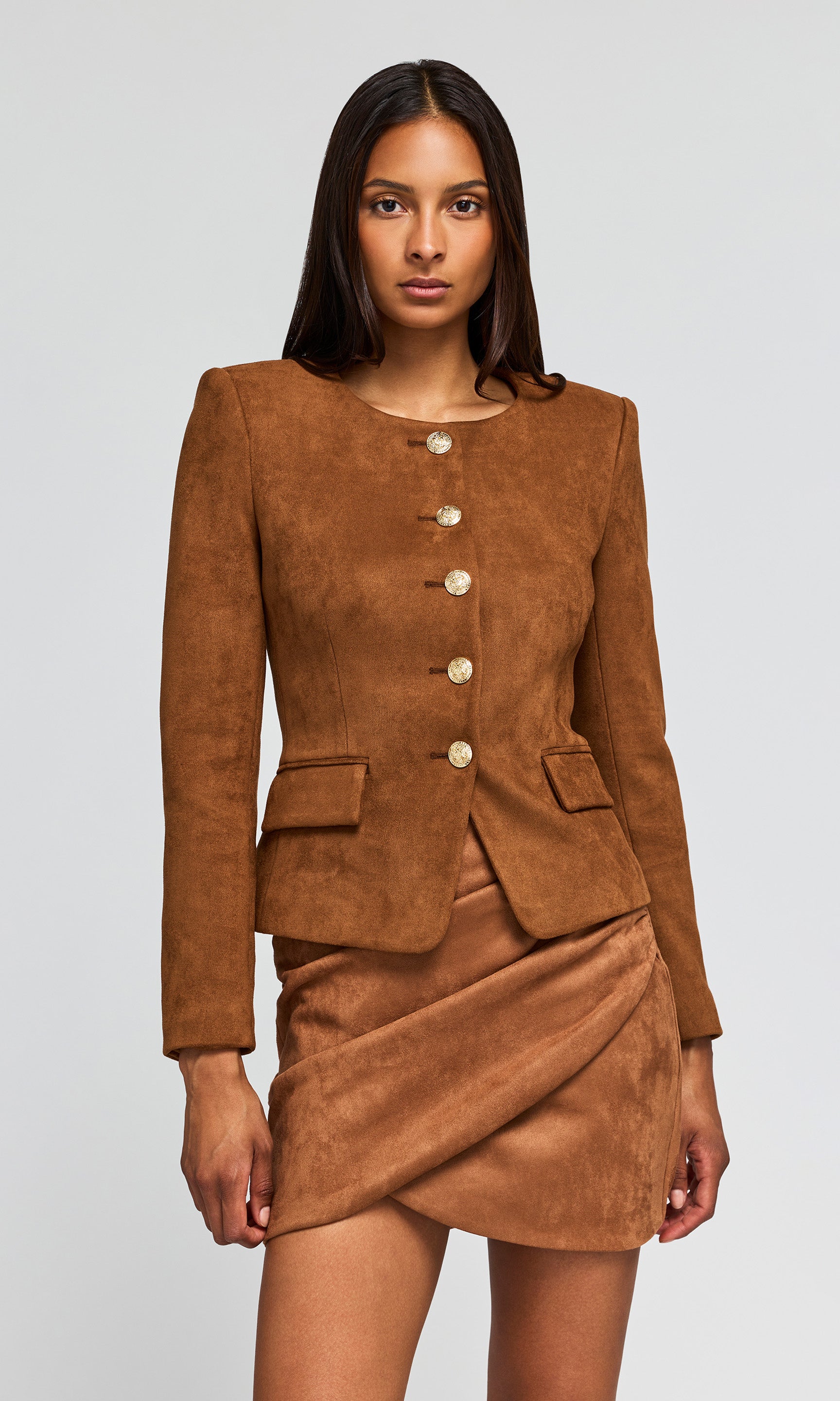Model wearing a brown suede-like two-piece suit consisting of a cropped jacket with gold buttons and a matching wrap skirt.