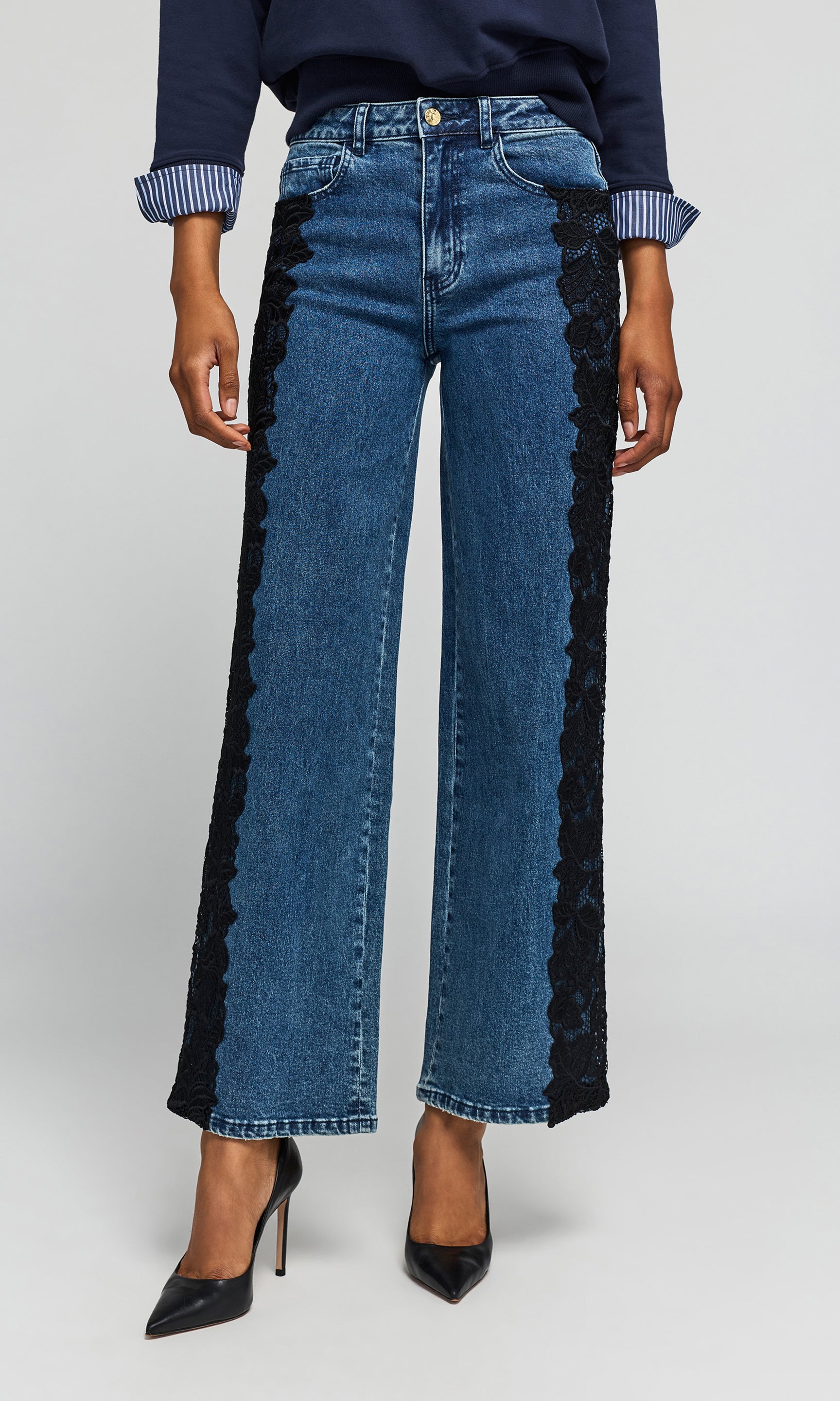 Model wearing a blue wide-leg jeans with black lace side panels, styled with a navy top and black heels.