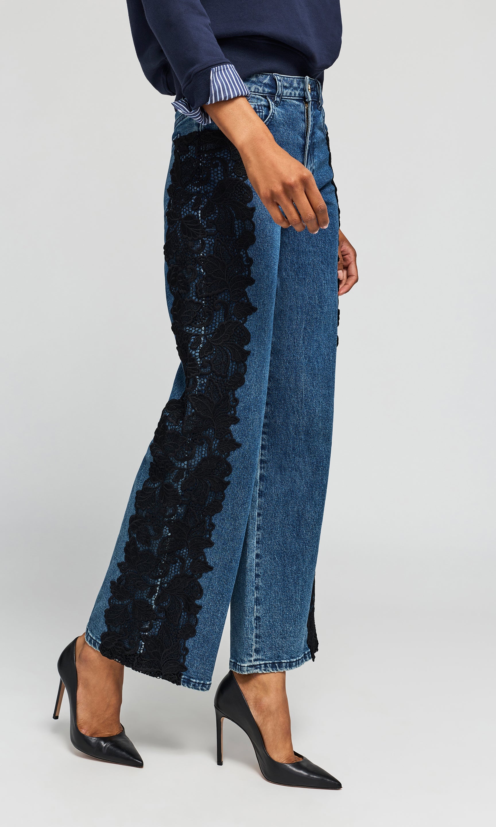 Side view of model wearing a blue wide-leg jeans with black lace side panels, styled with a navy top and black heels.