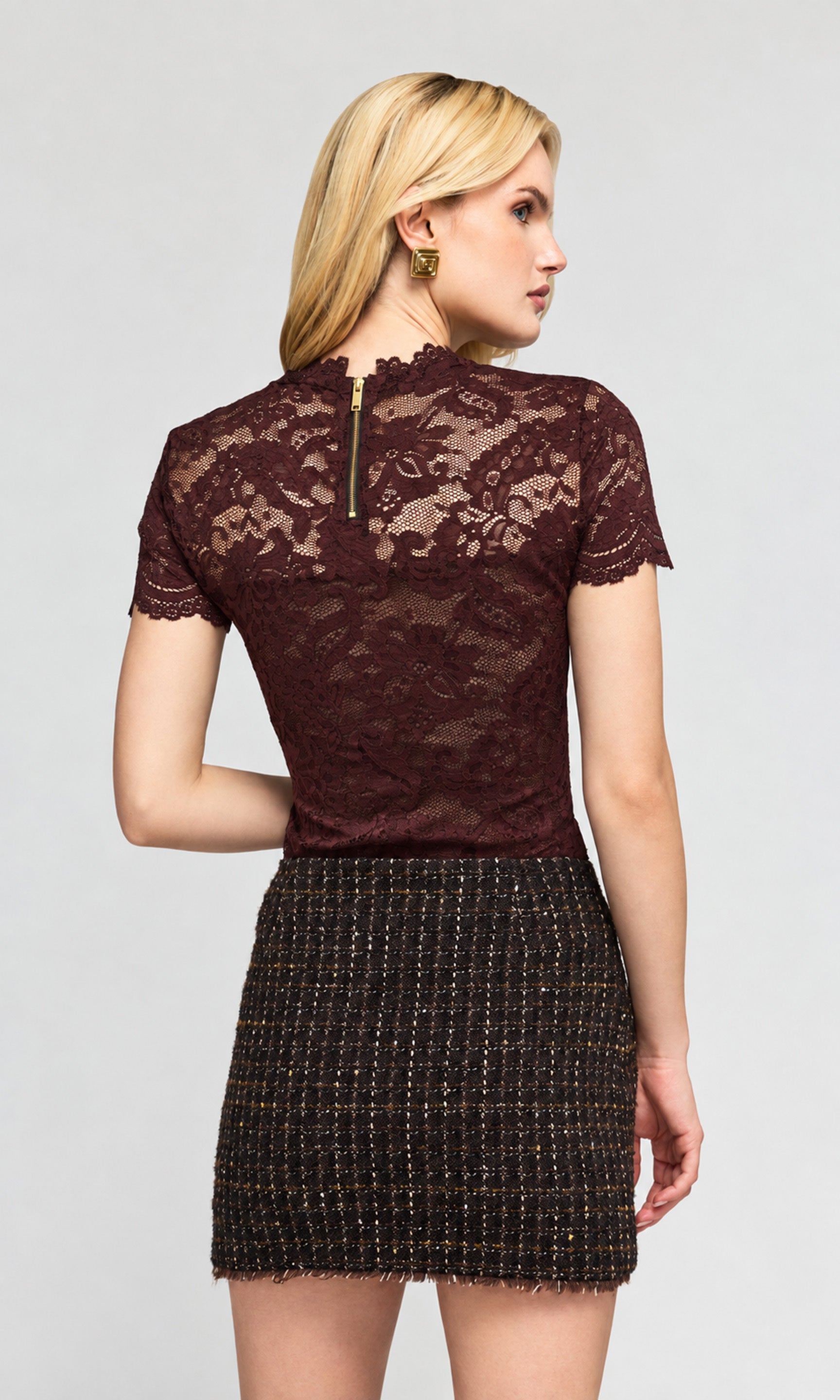 Back view of model wearing a short-sleeve burgundy lace top and a black tweed mini skirt.