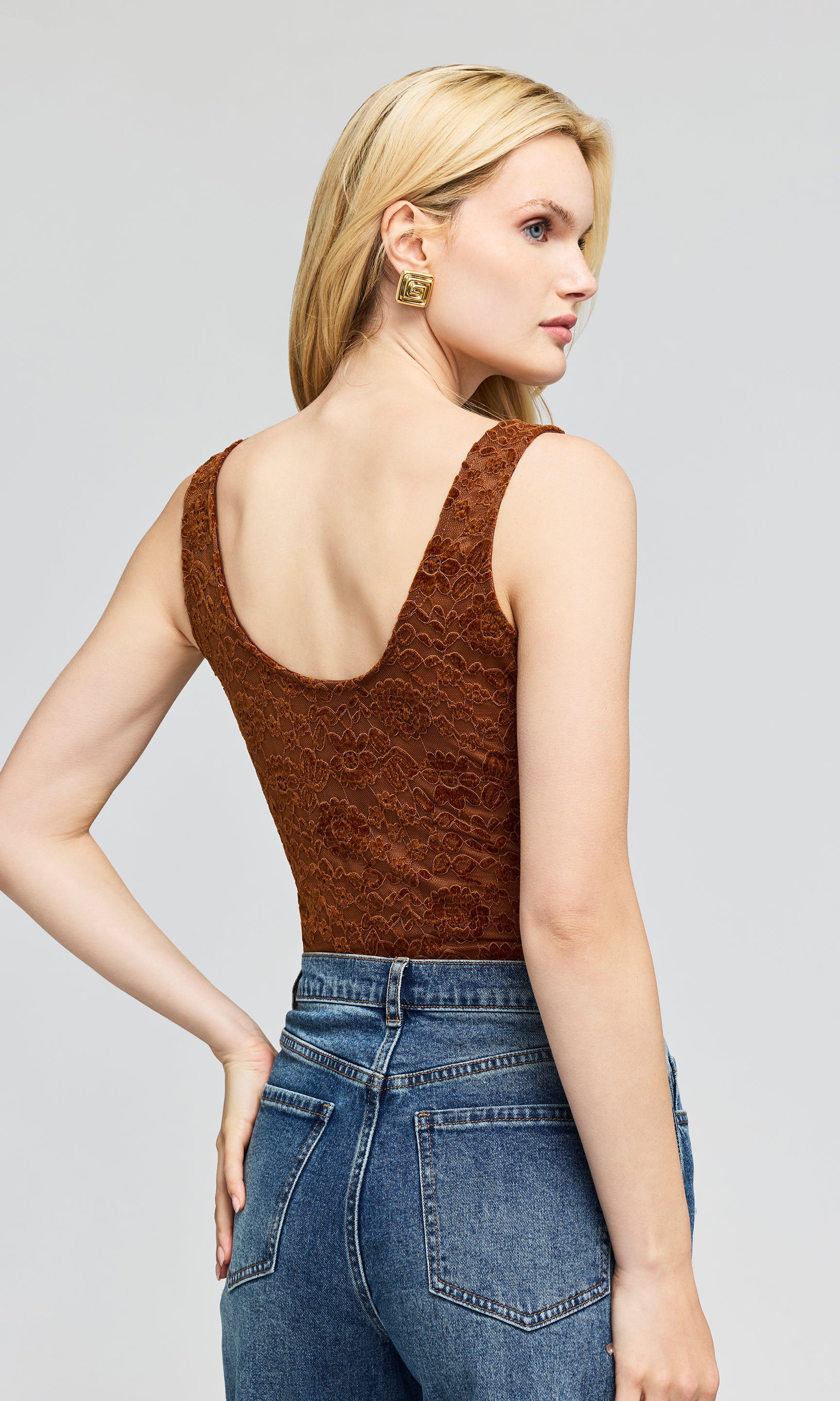 Back view of model wearing a brown lace camisole top and blue jeans, standing on a plain background.