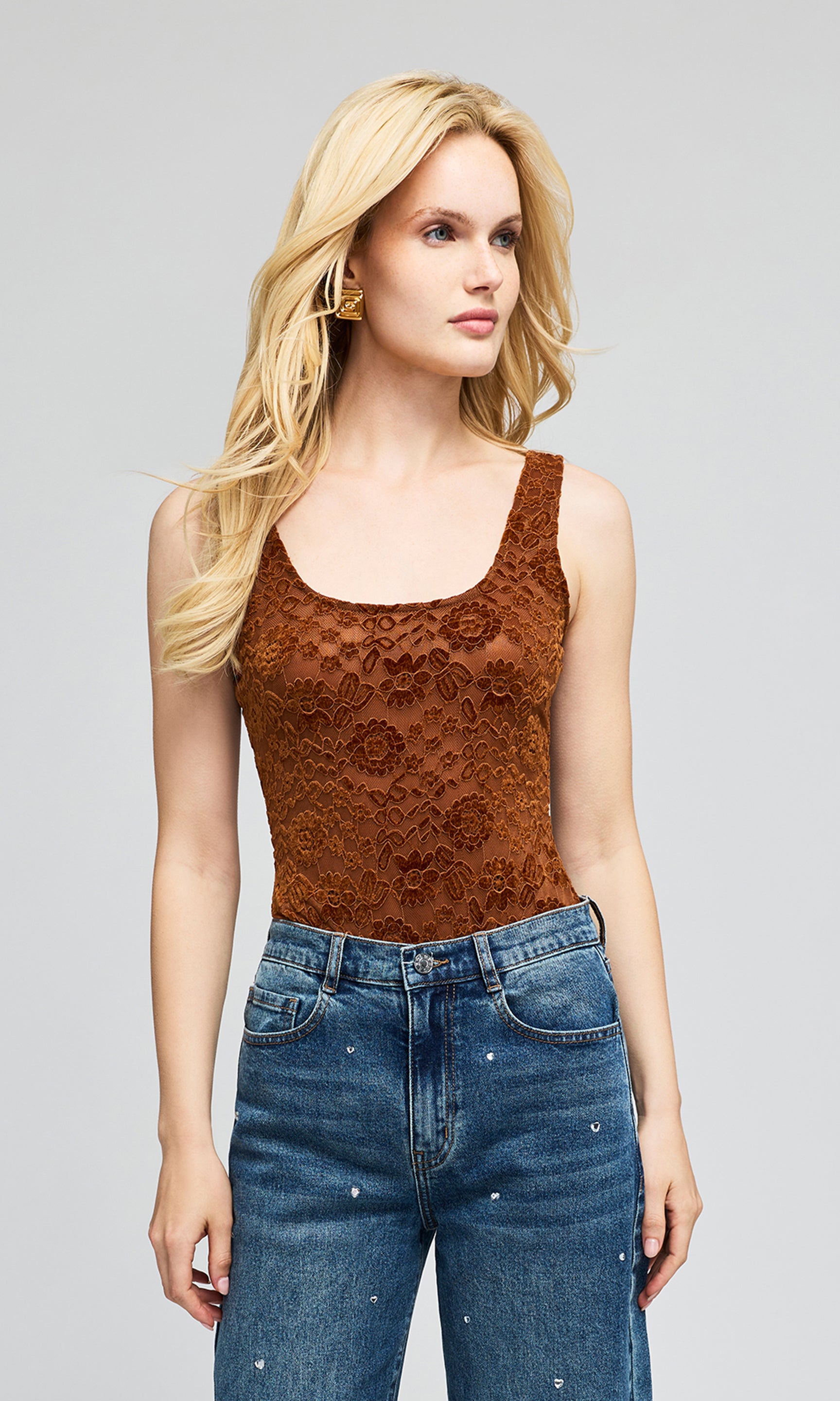 Model wearing a brown lace camisole top and blue jeans, standing on a plain background.