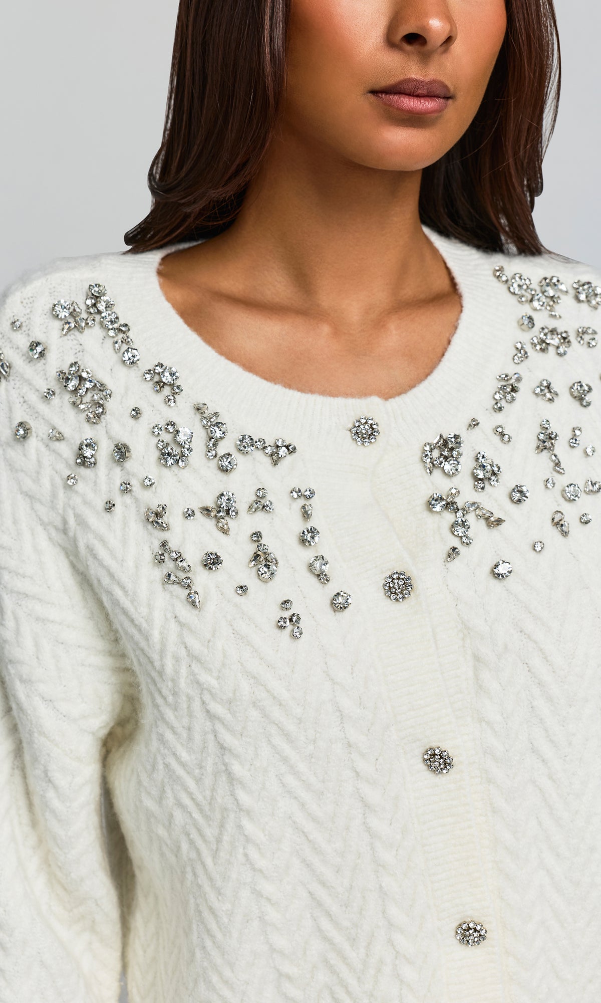 Close-up of a woman wearing a cream cable-knit sweater with silver rhinestone embellishments around the neckline and down the front.