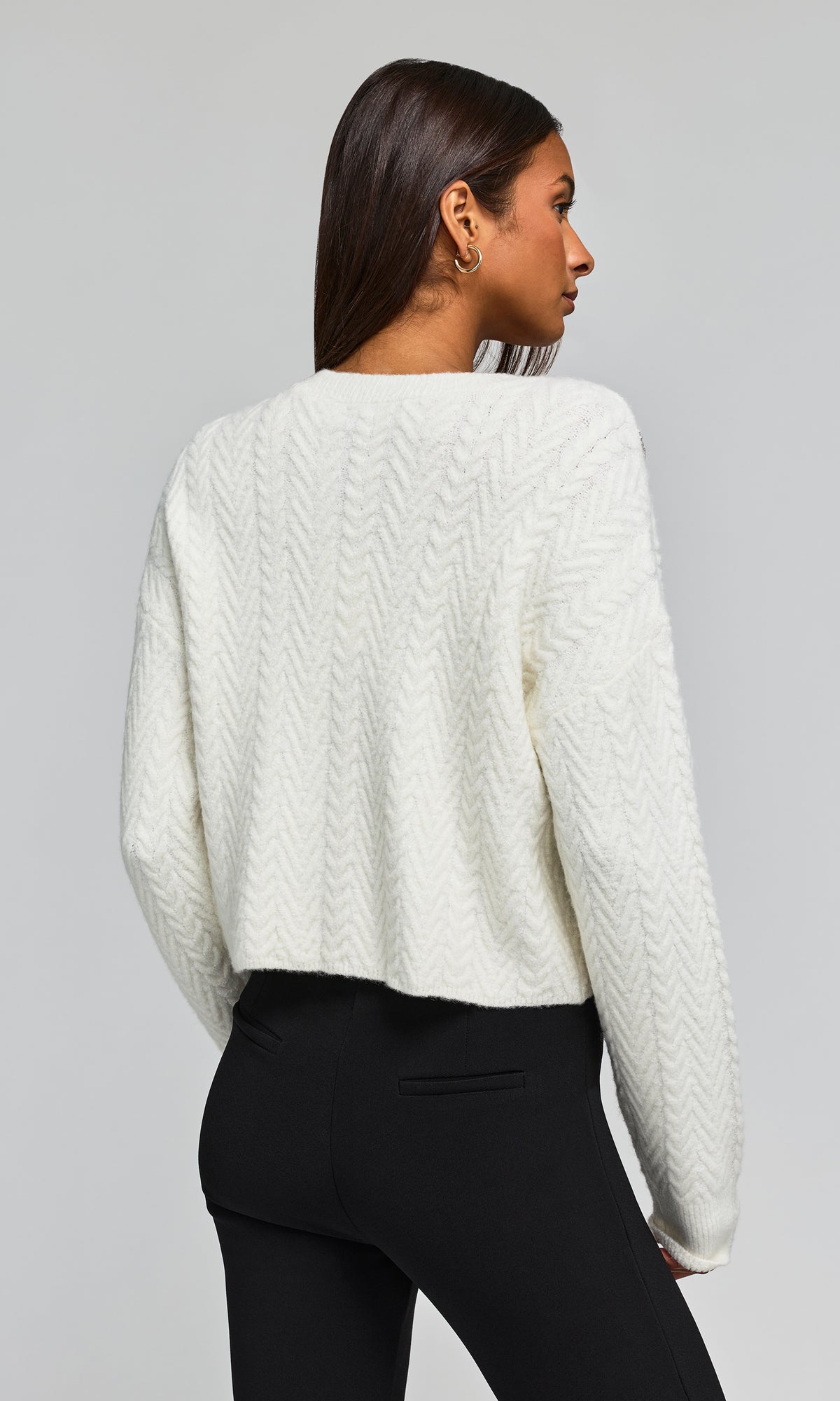 Back view of model wearing a cream-colored textured knit sweater and black pants.
