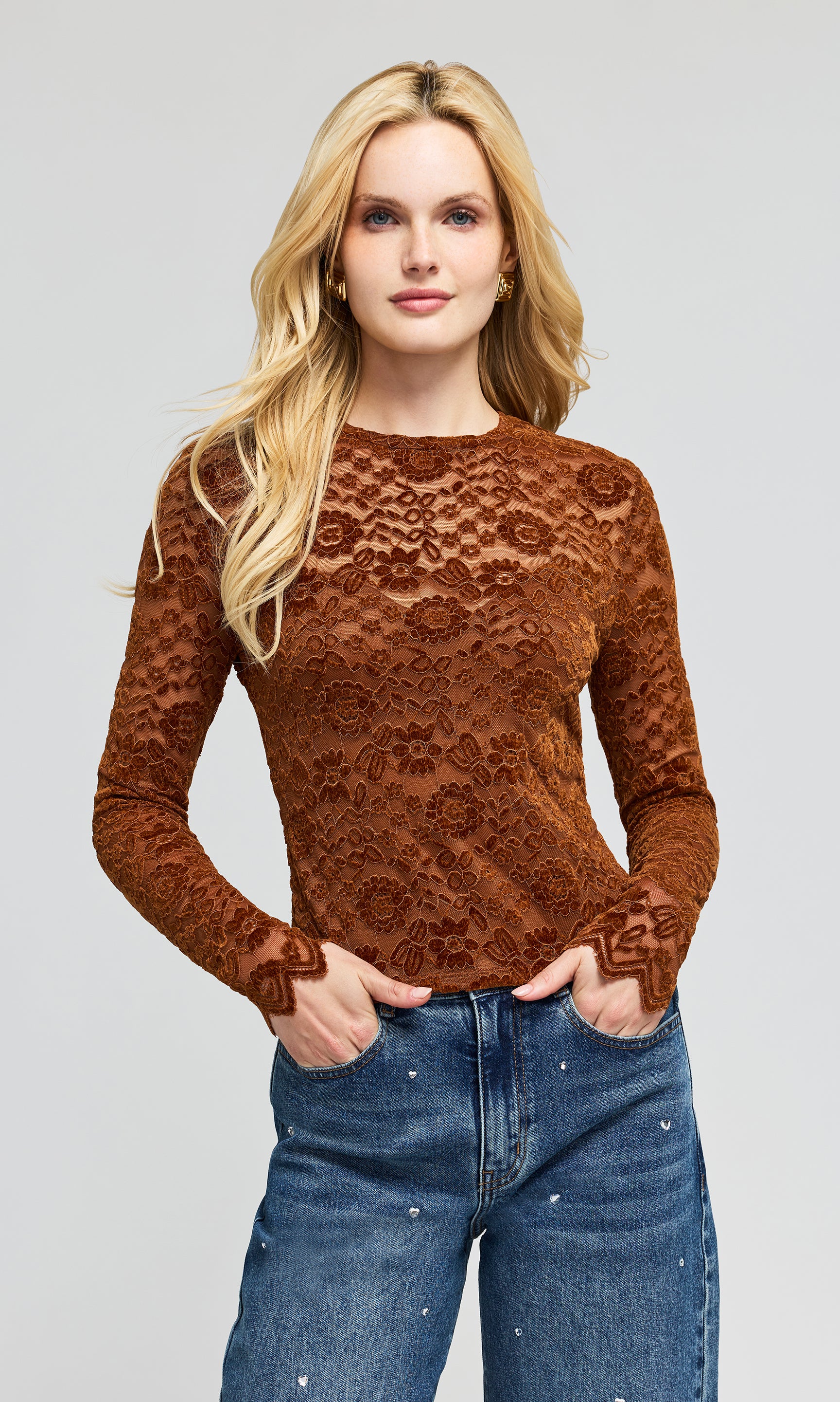 Model wearing a brown lace long-sleeve top and blue jeans, standing on a plain background.