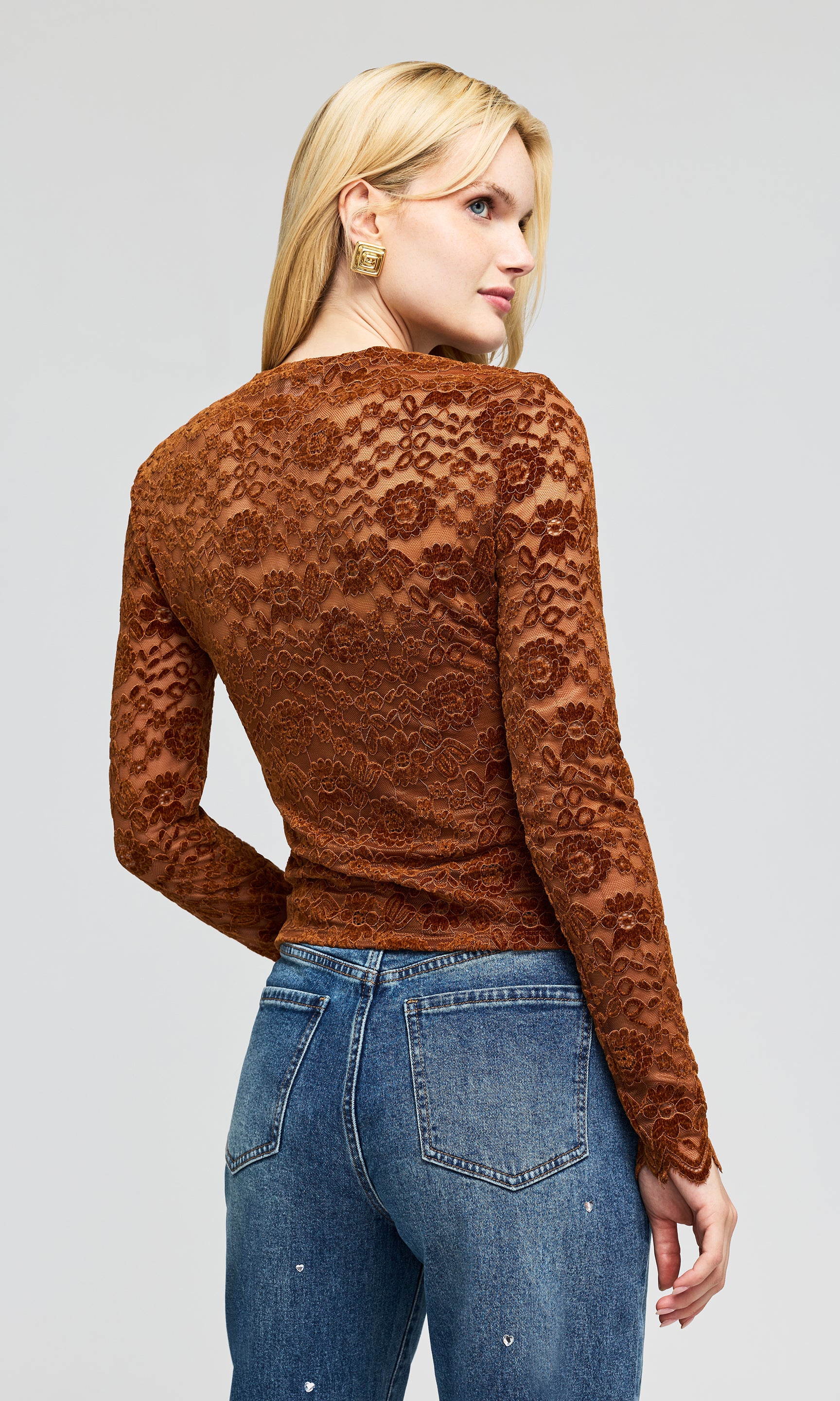 Back view of model wearing a brown lace long-sleeve top and blue jeans, standing on a plain background.