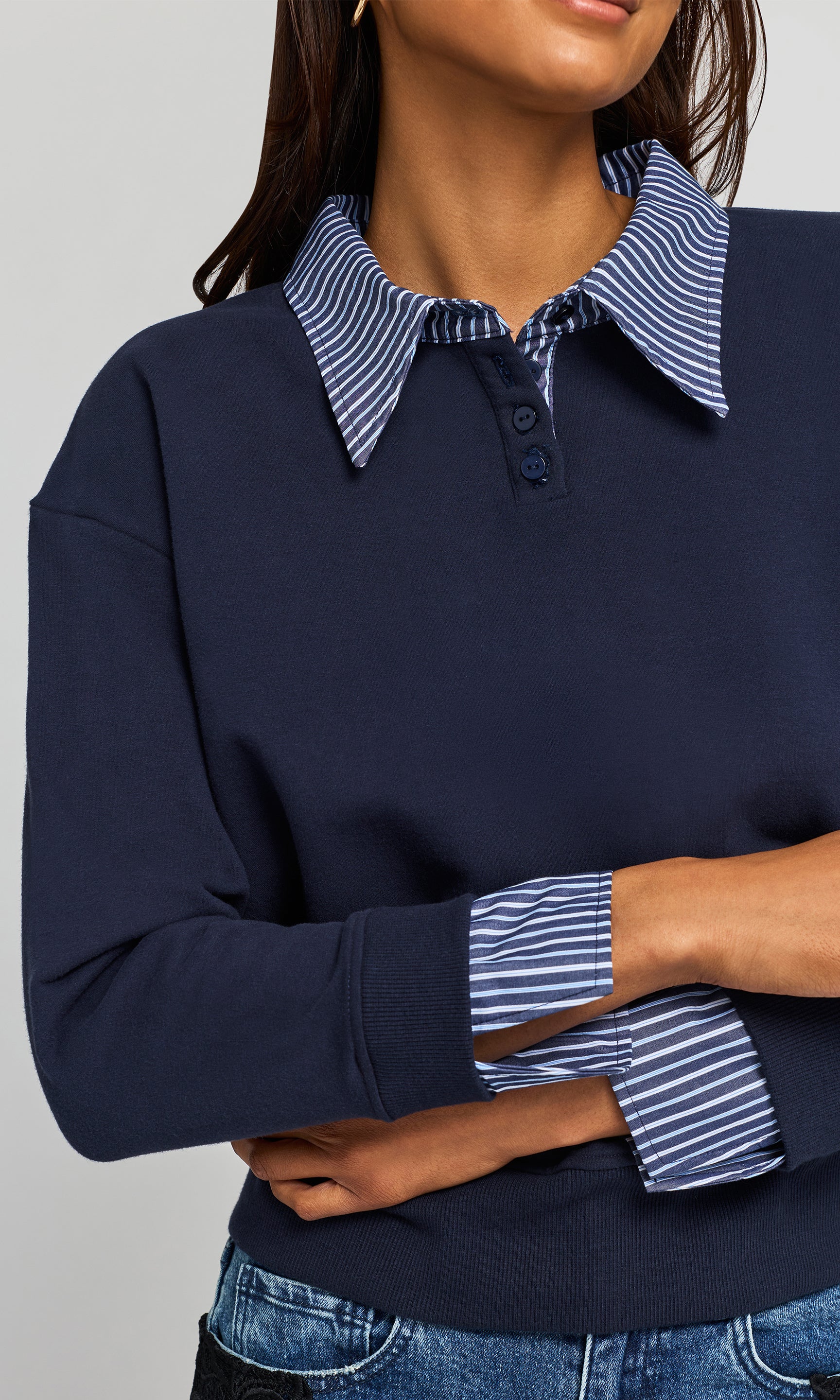 Close-up of model wearing a navy long-sleeve knit top with a blue and white striped polo-style collar shirt against a light gray background.