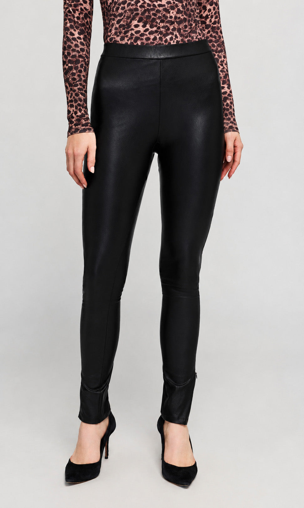 Black faux-leather leggings worn by a model, paired with a leopard-print long-sleeve top on a plain background.