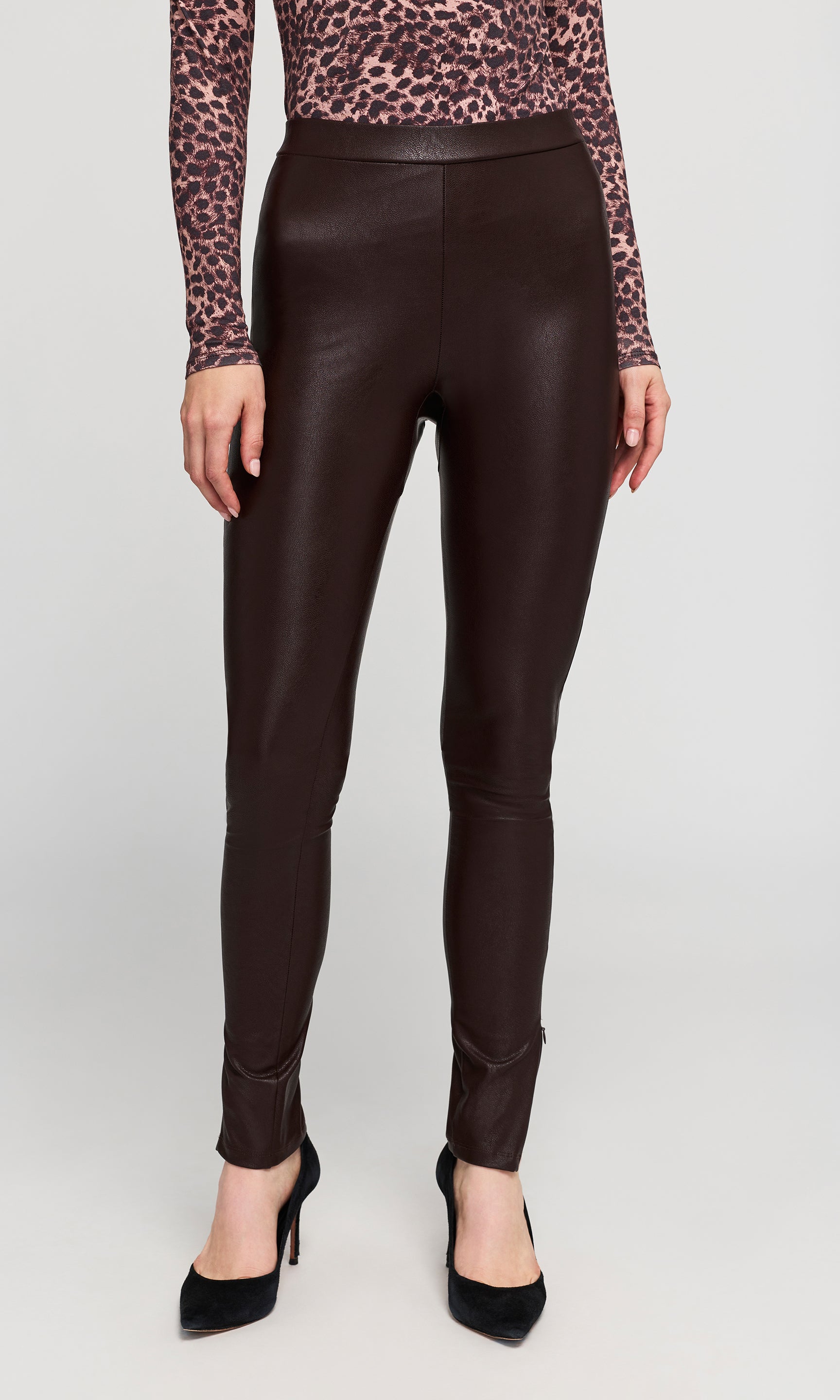 A model wearing dark brown faux-leather leggings with a leopard-print long-sleeve top on a plain background.