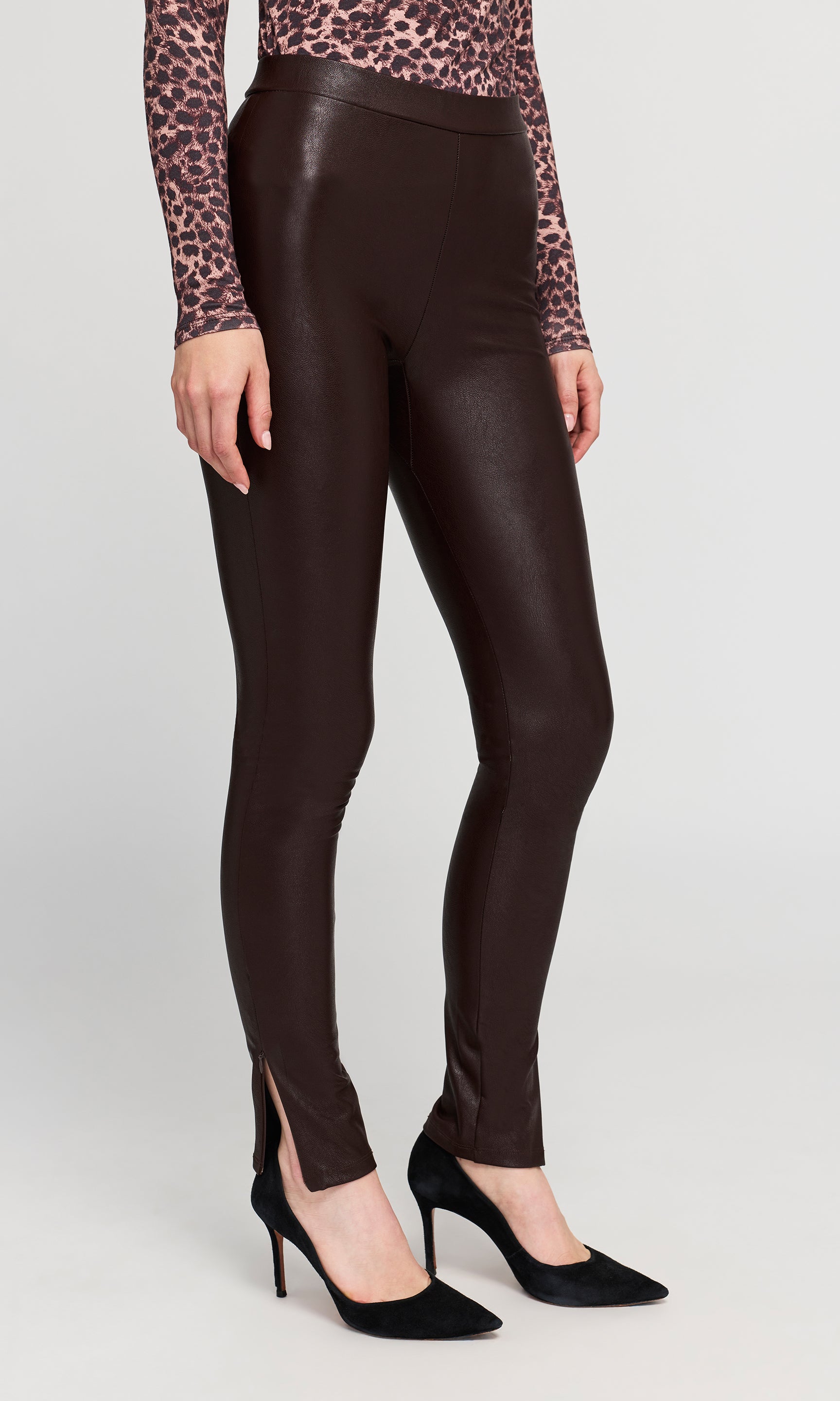Side view of model wearing dark brown faux-leather leggings with a leopard-print long-sleeve top on a plain background.