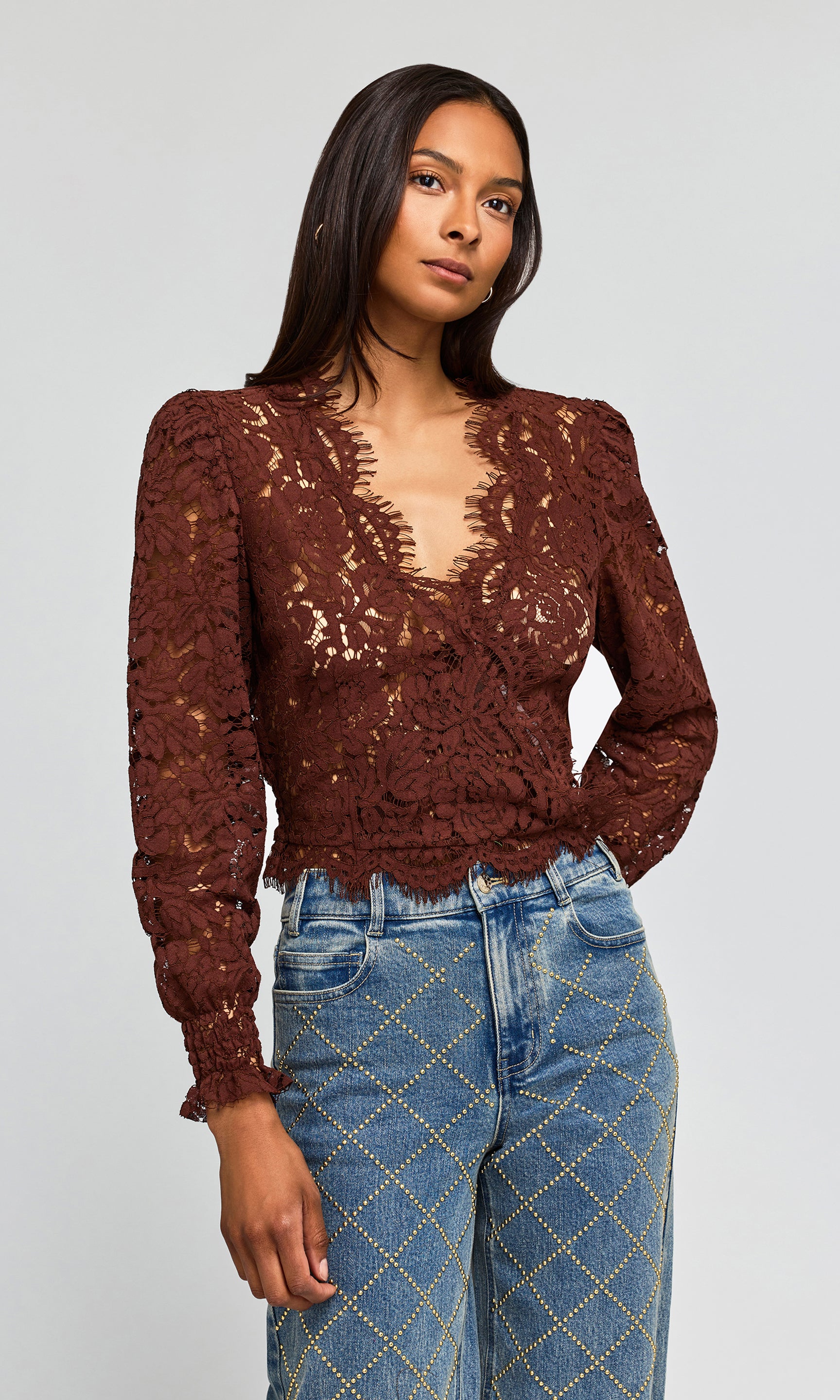 Side view of model wearing a dark brown lace long-sleeve crop top and blue jeans.