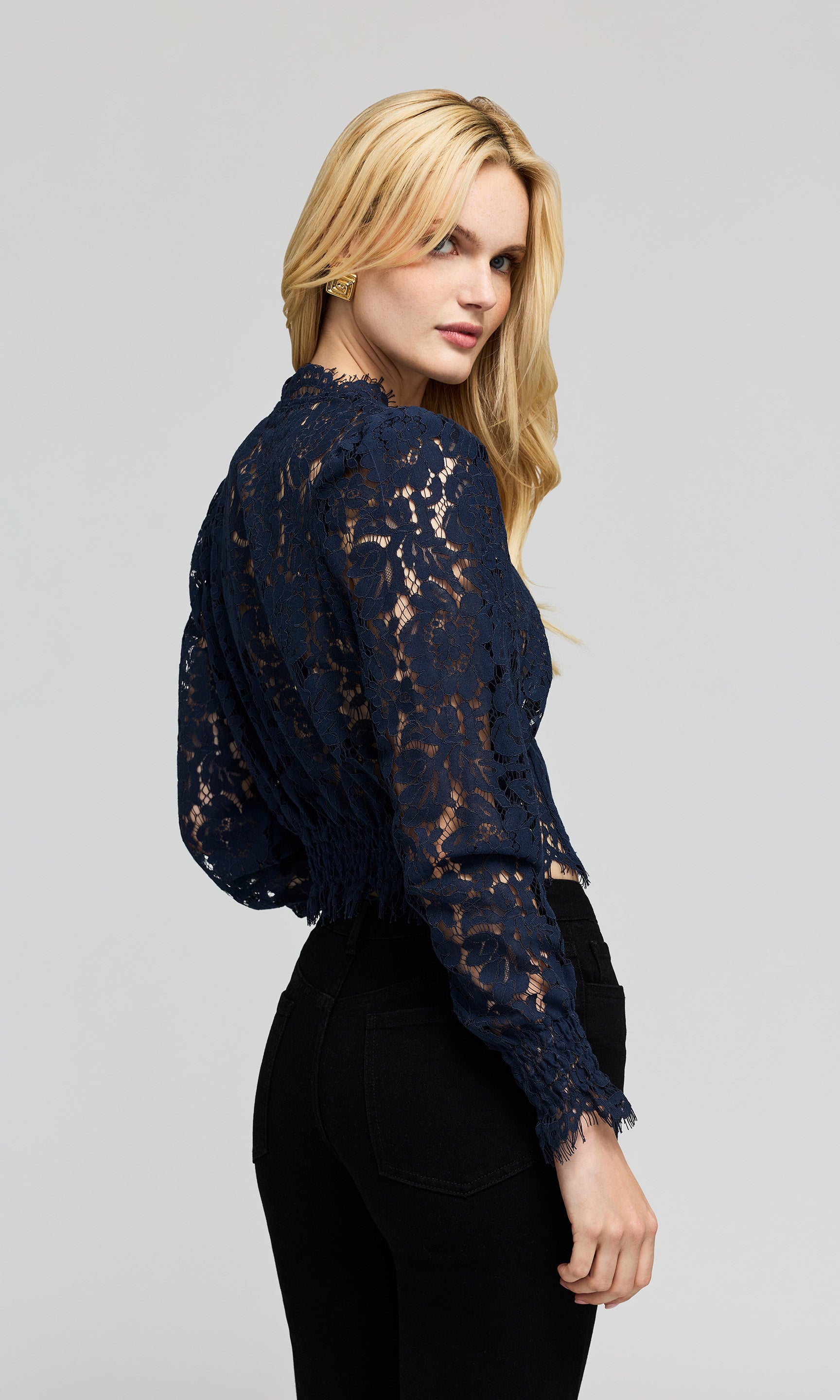 Model wearing a navy blue lace long-sleeve blouse with a high neck, shown from a three-quarters back view.