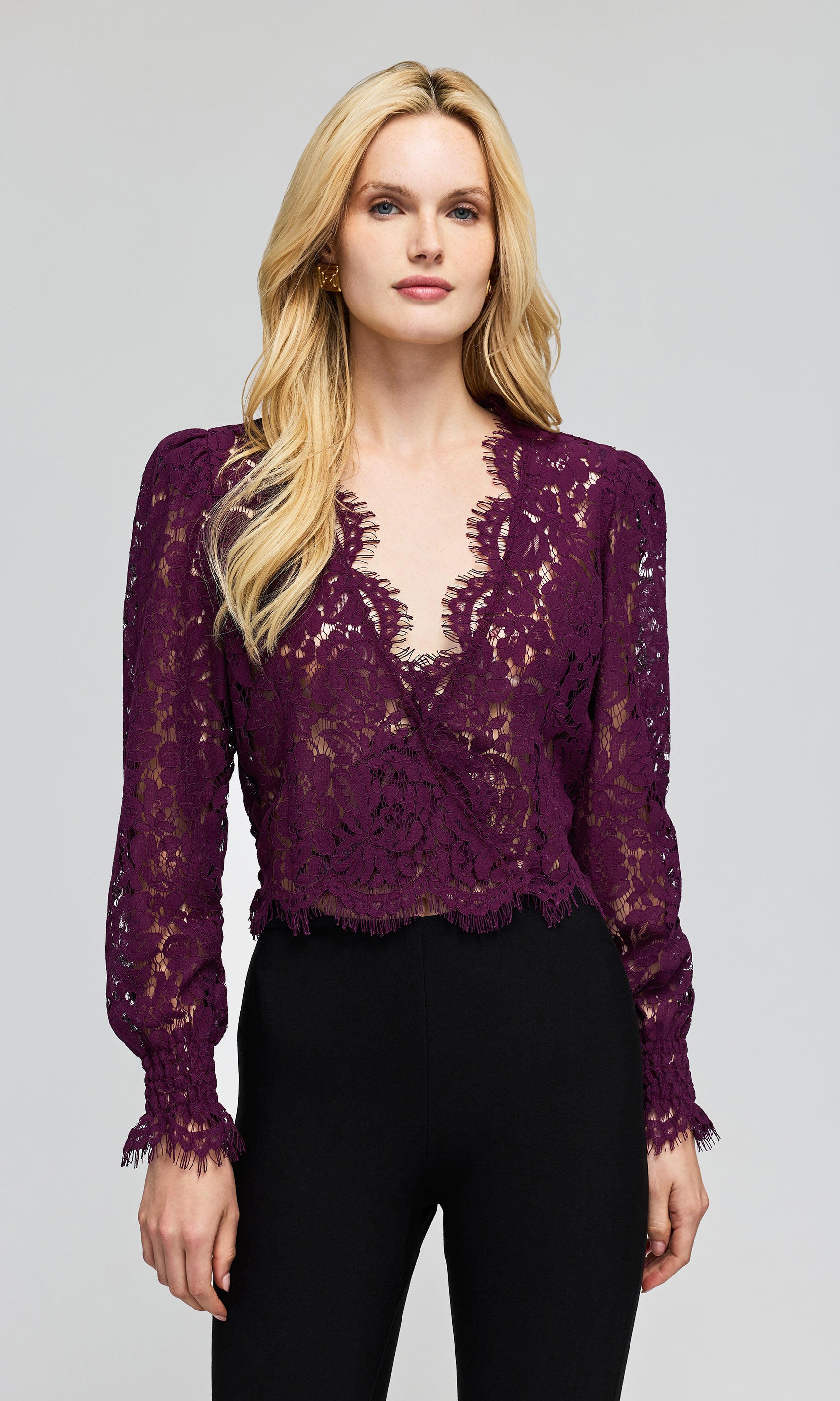 Model wearing a deep purple lace long-sleeve blouse with a deep V-neck and black pants, on a plain background.
