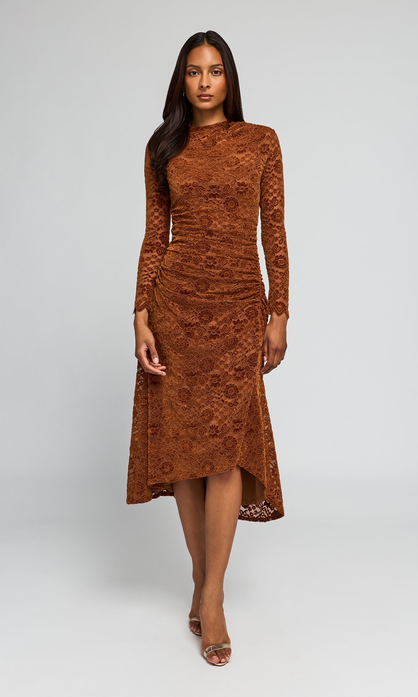 A woman modeling a rust-brown long-sleeve lace midi dress with a high-low hem.