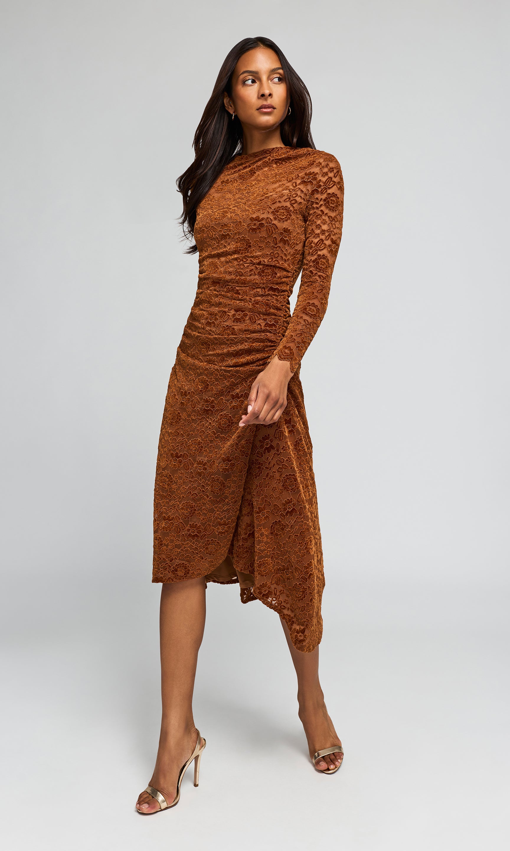 Side view of a woman modeling a rust-brown long-sleeve lace midi dress with a high-low hem.