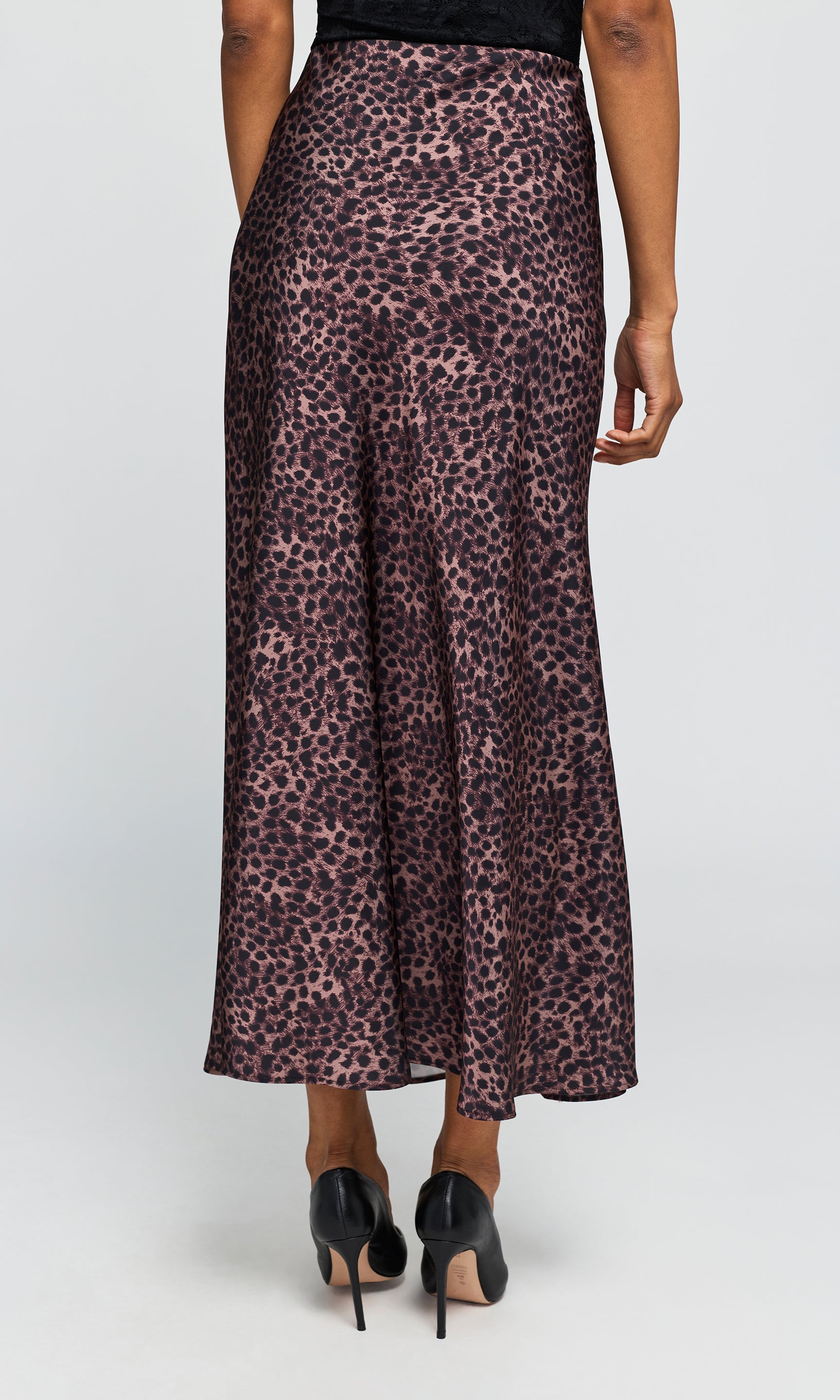 Back view of model wearing a high-waisted, floor-length leopard print skirt, paired with black pointed-toe heels on a plain background.