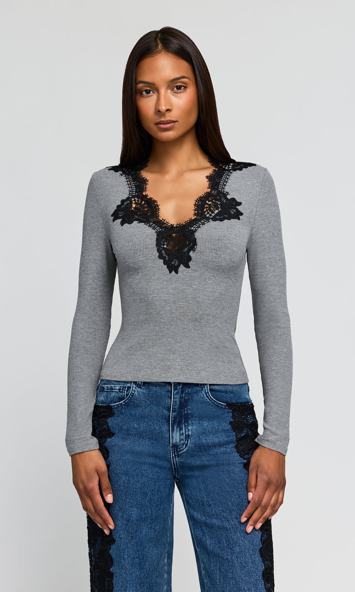 Model wearing a fitted long-sleeve gray top with black lace trim around the scoop neckline, paired with blue jeans featuring black lace side panels.