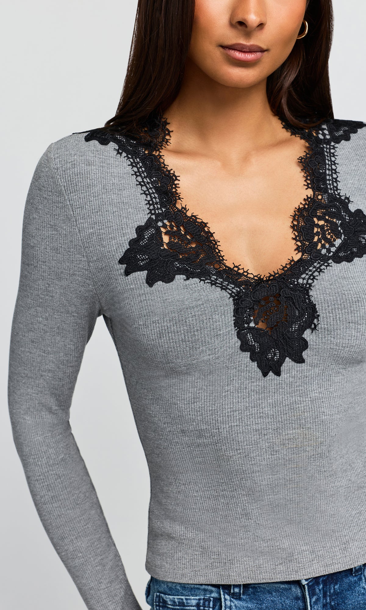 Close-up of a fitted heather gray long-sleeve top with a black lace V-neckline detail, paired with blue jeans..