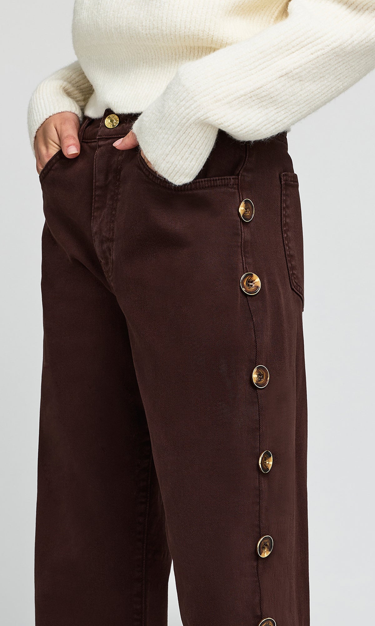 A close-up of a person wearing dark brown wide-leg pants with a vertical row of large gold-tone buttons down the side.
