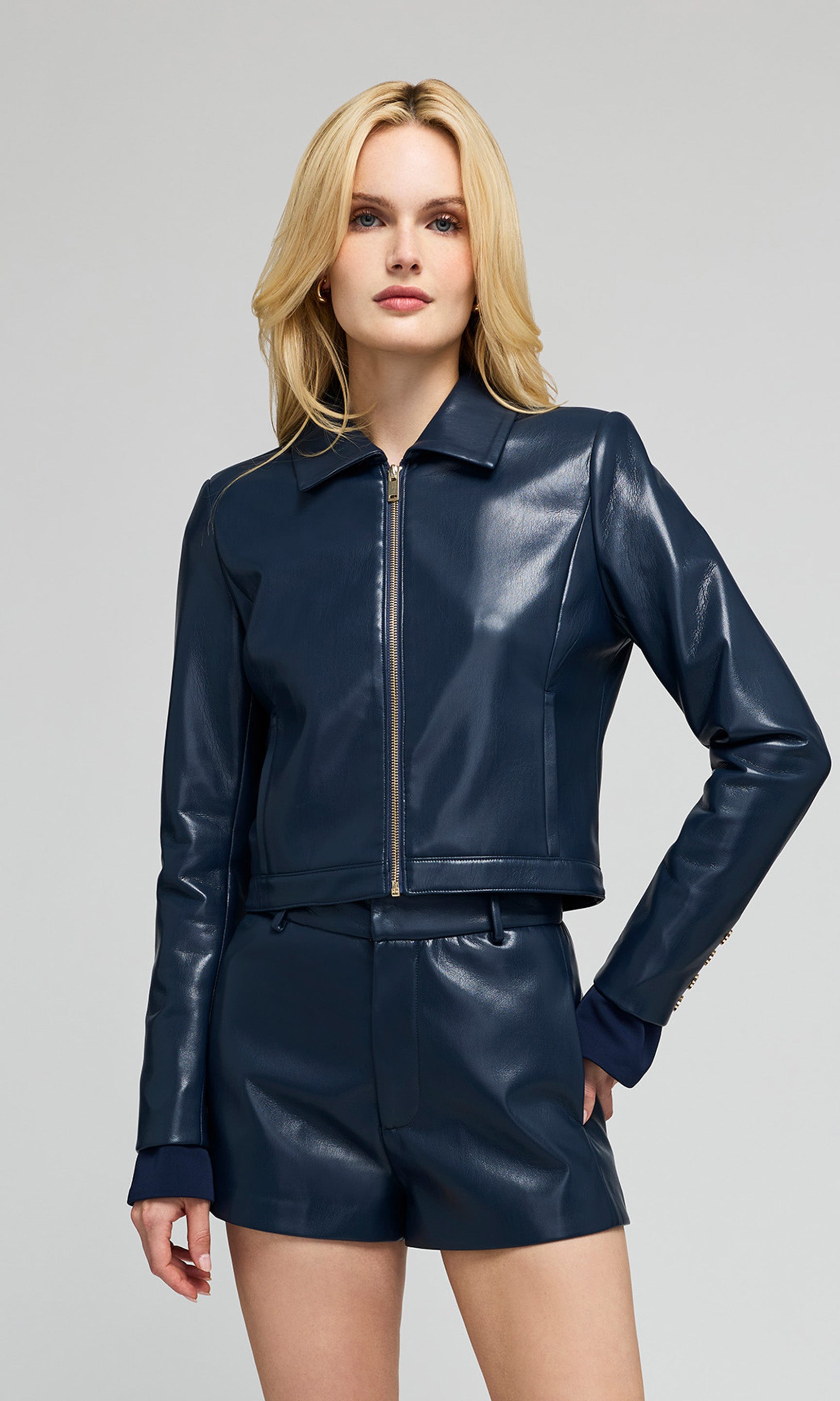 Model wearing a blue faux-leather jacket with a front zipper and matching shorts with a plain background.