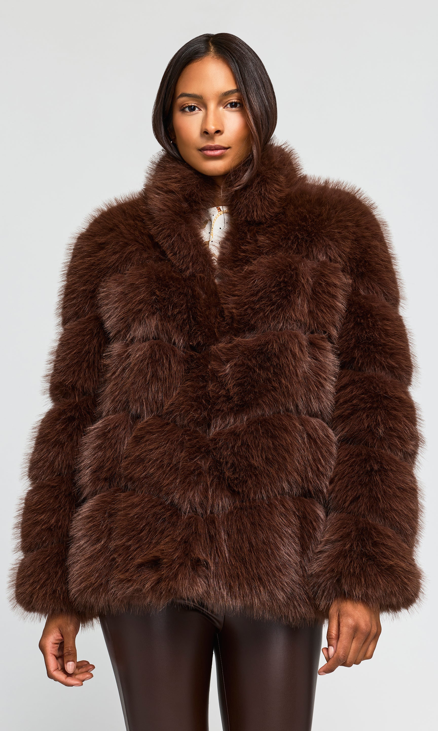 A woman modeling a dark brown faux fur jacket with a high collar, set against a plain light gray studio background.