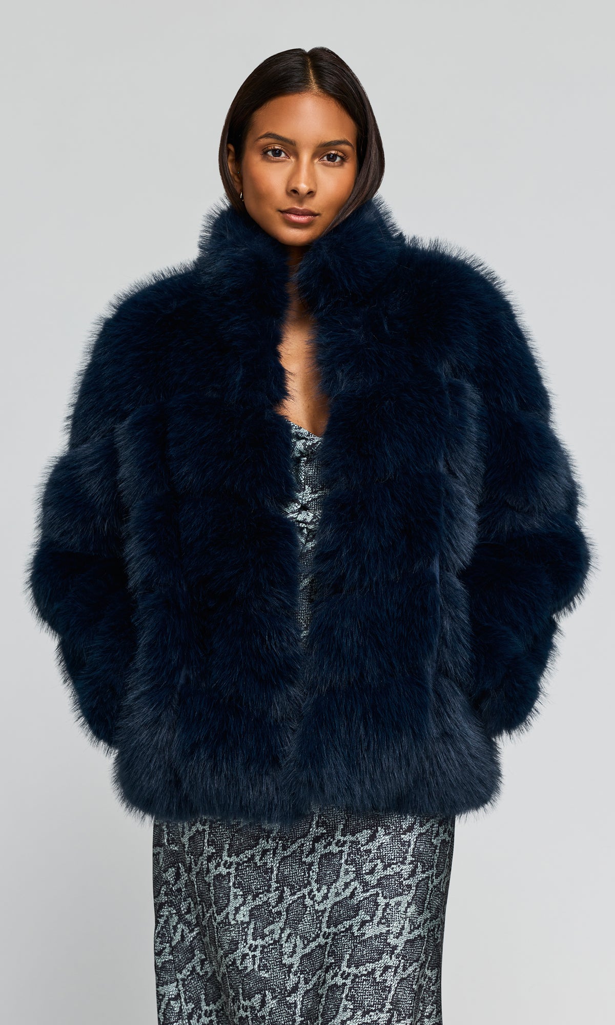 Model wearing a voluminous, dark navy blue faux fur jacket over a snake patterned gray dress.