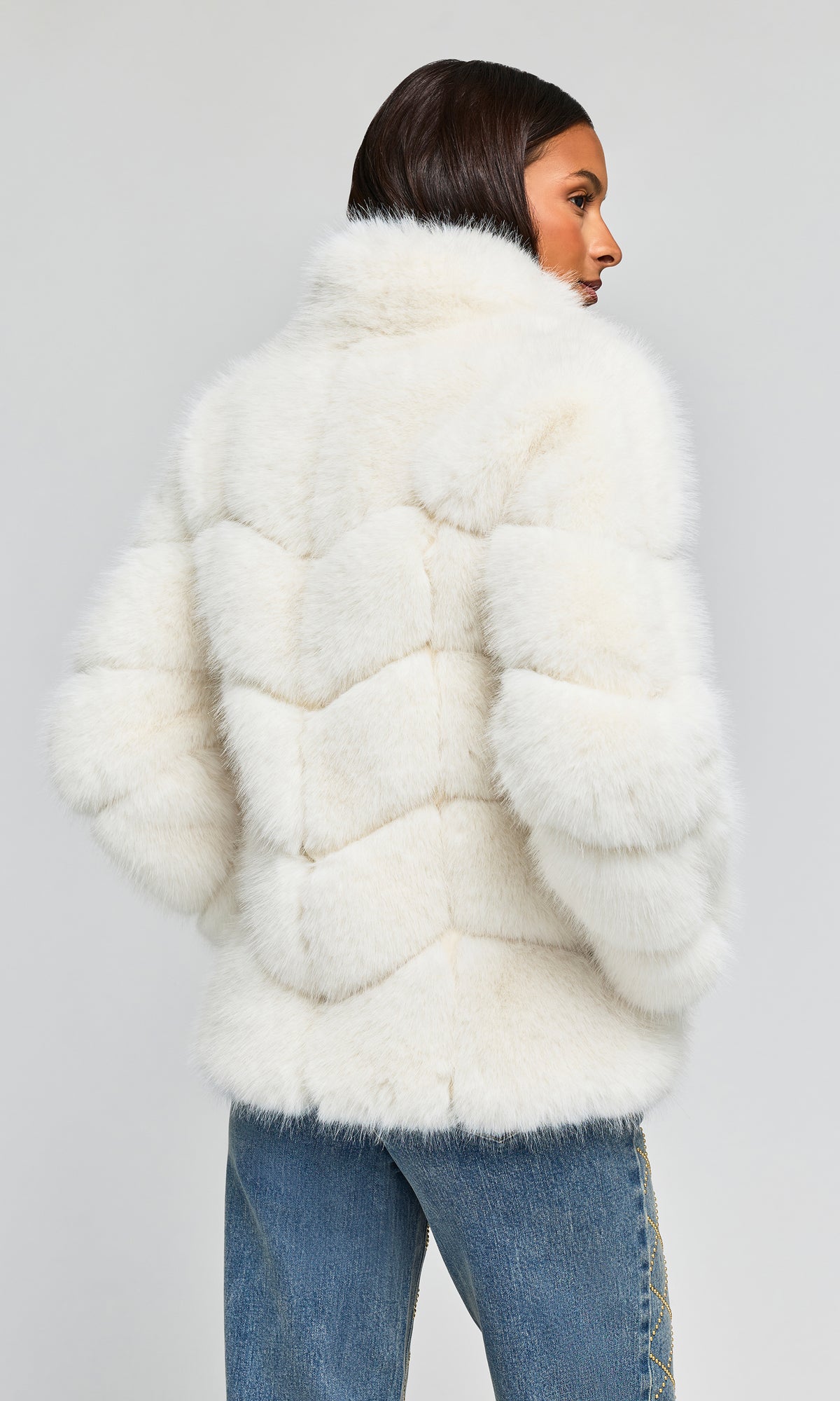 Back view of model wearing a voluminous, textured white faux fur jacket with padded chevron details and a high collar.