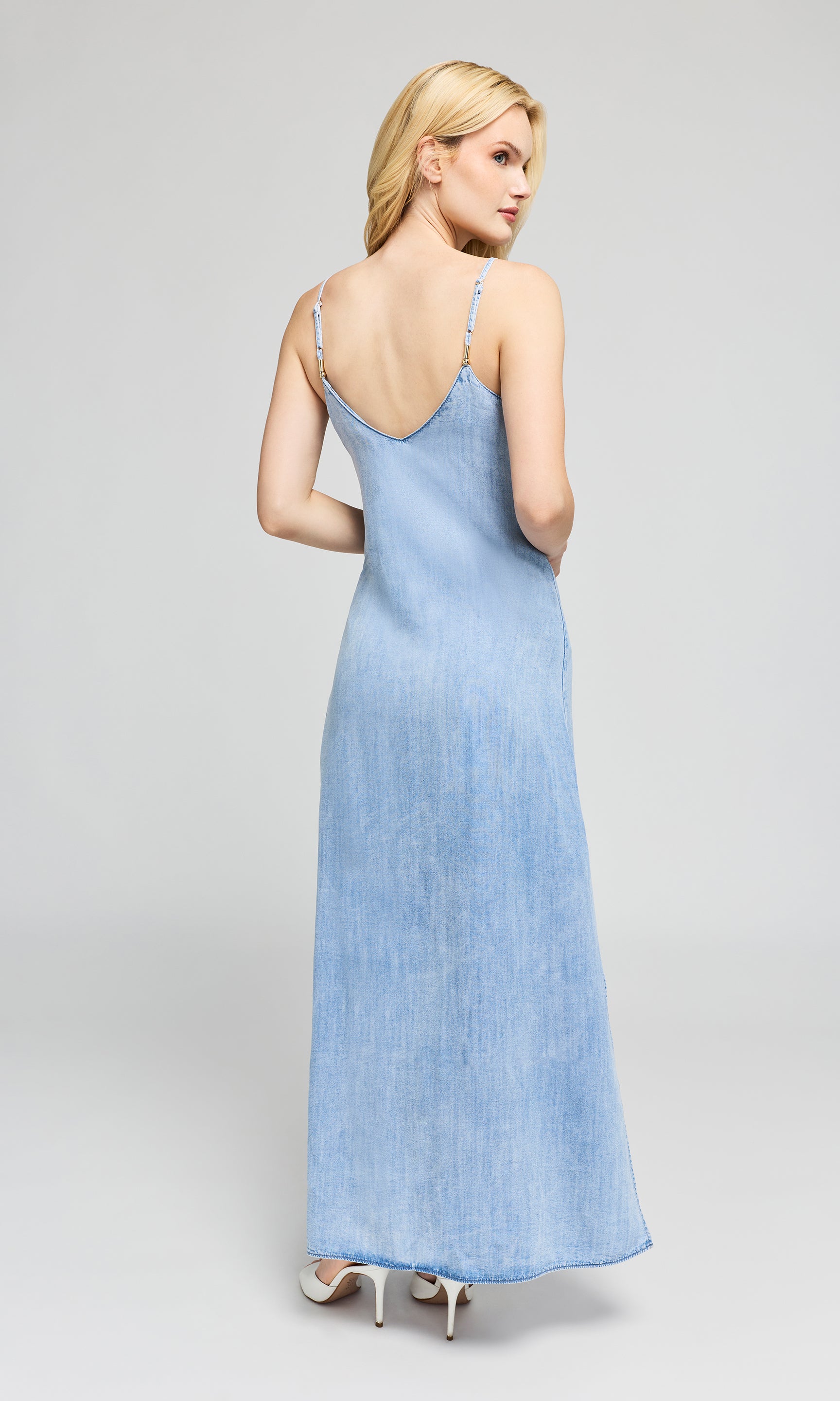 Back view of woman wearing a light blue dress with thin straps on a gray background