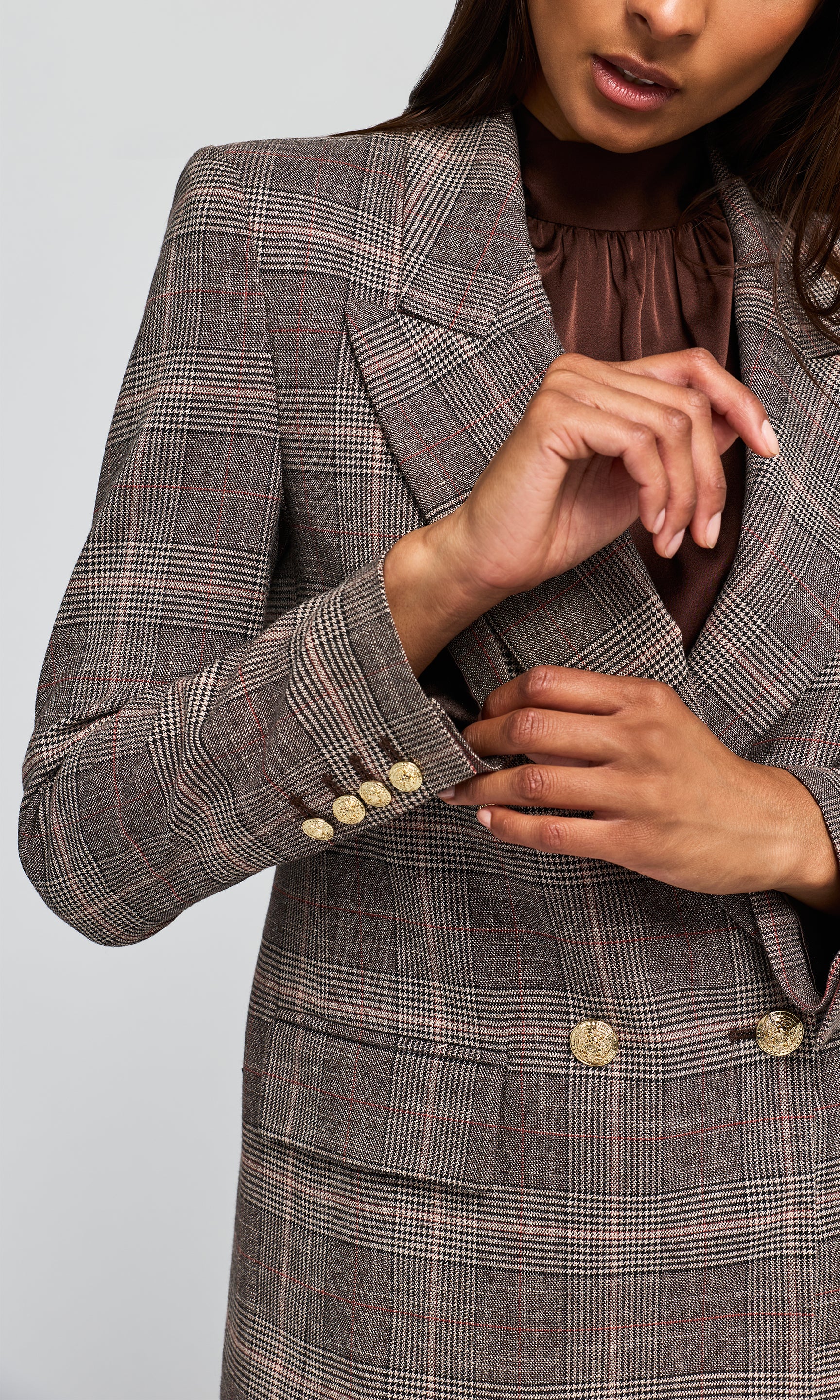 Close-up of a tailored plaid blazer in brown, beige, and gray tones, with gold-tone buttons.