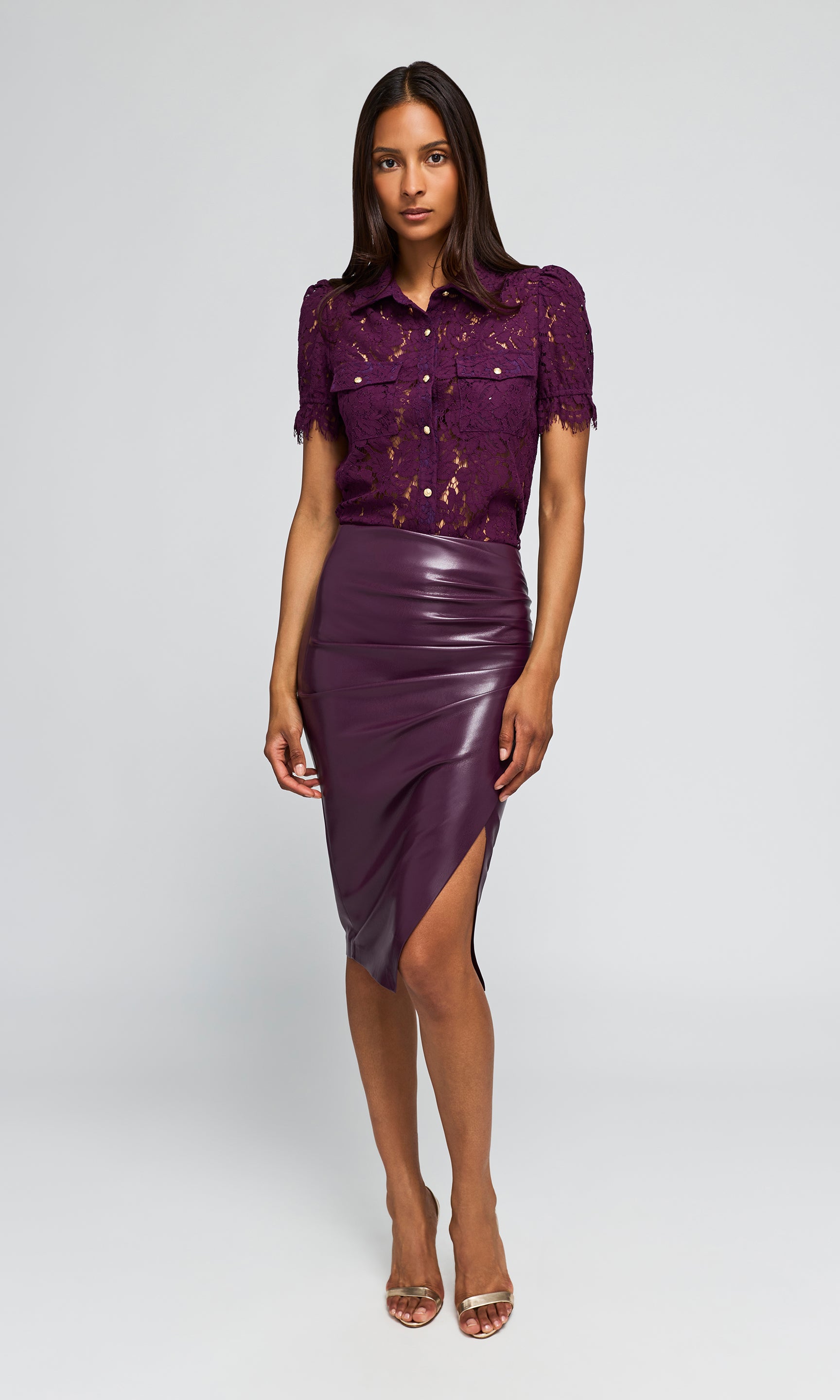 Model wearing a short-sleeve purple shirt and a matching faux-leather wrap skirt, paired with gold heels.