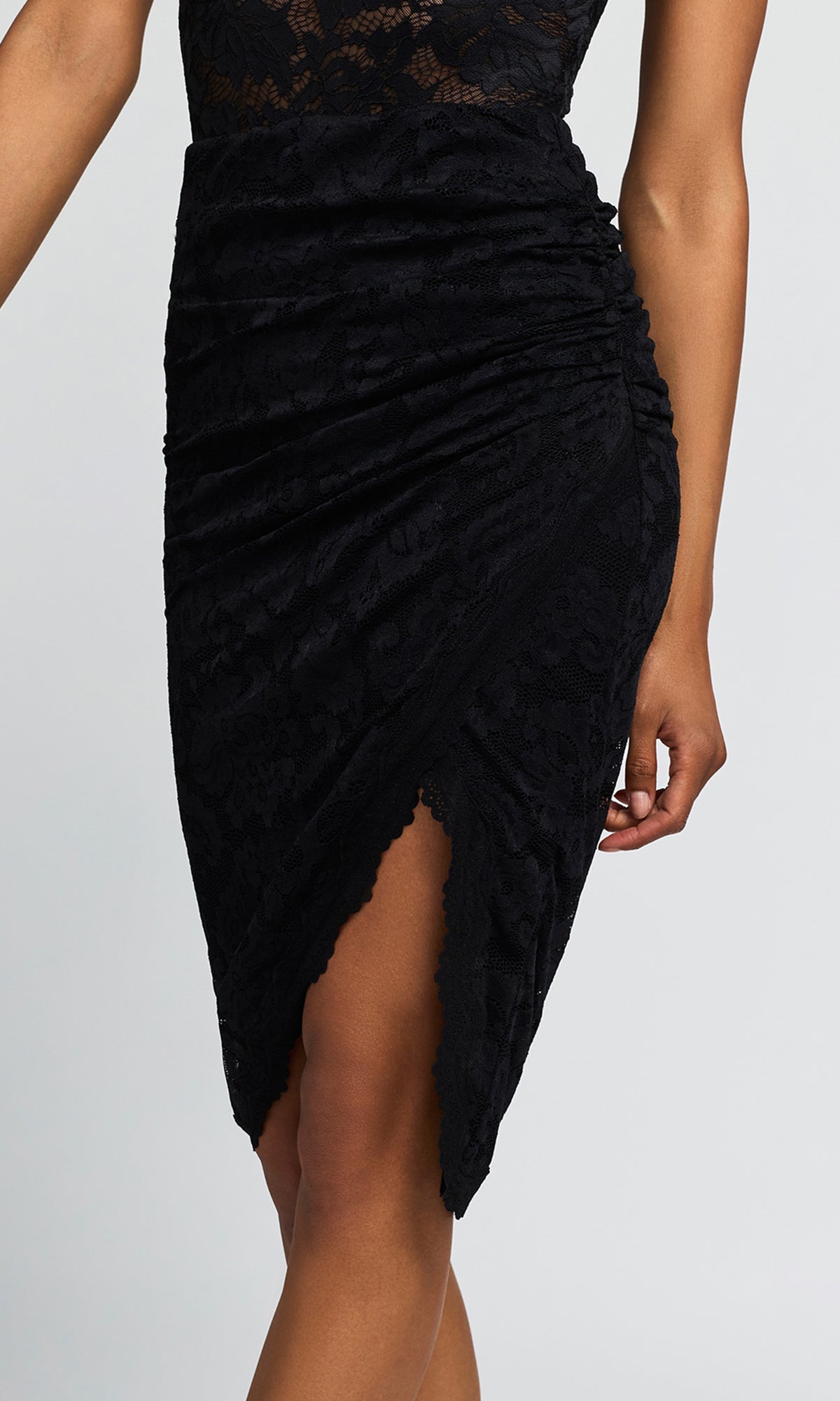 A close-up of a model wearing a black ruched velvet midi skirt with a lace bodice and a high slit.