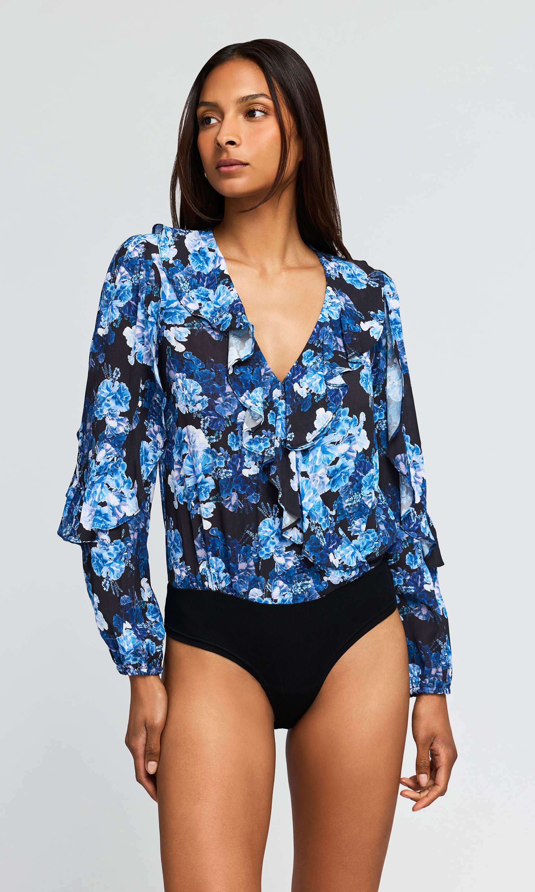 A woman modeling a long-sleeve floral bodysuit with a deep V-neck and black bikini bottoms.