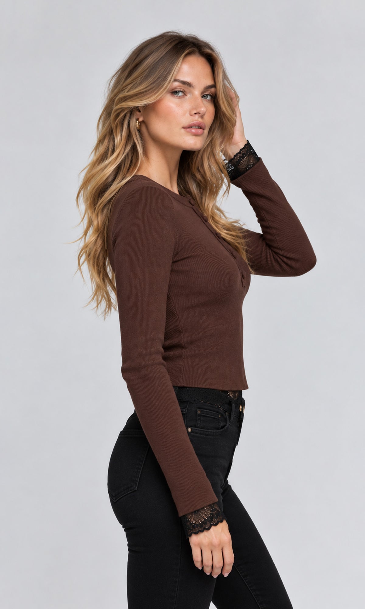 Side view of model wearing a fitted long-sleeve brown knit top with black lace cuffs, paired with black jeans.