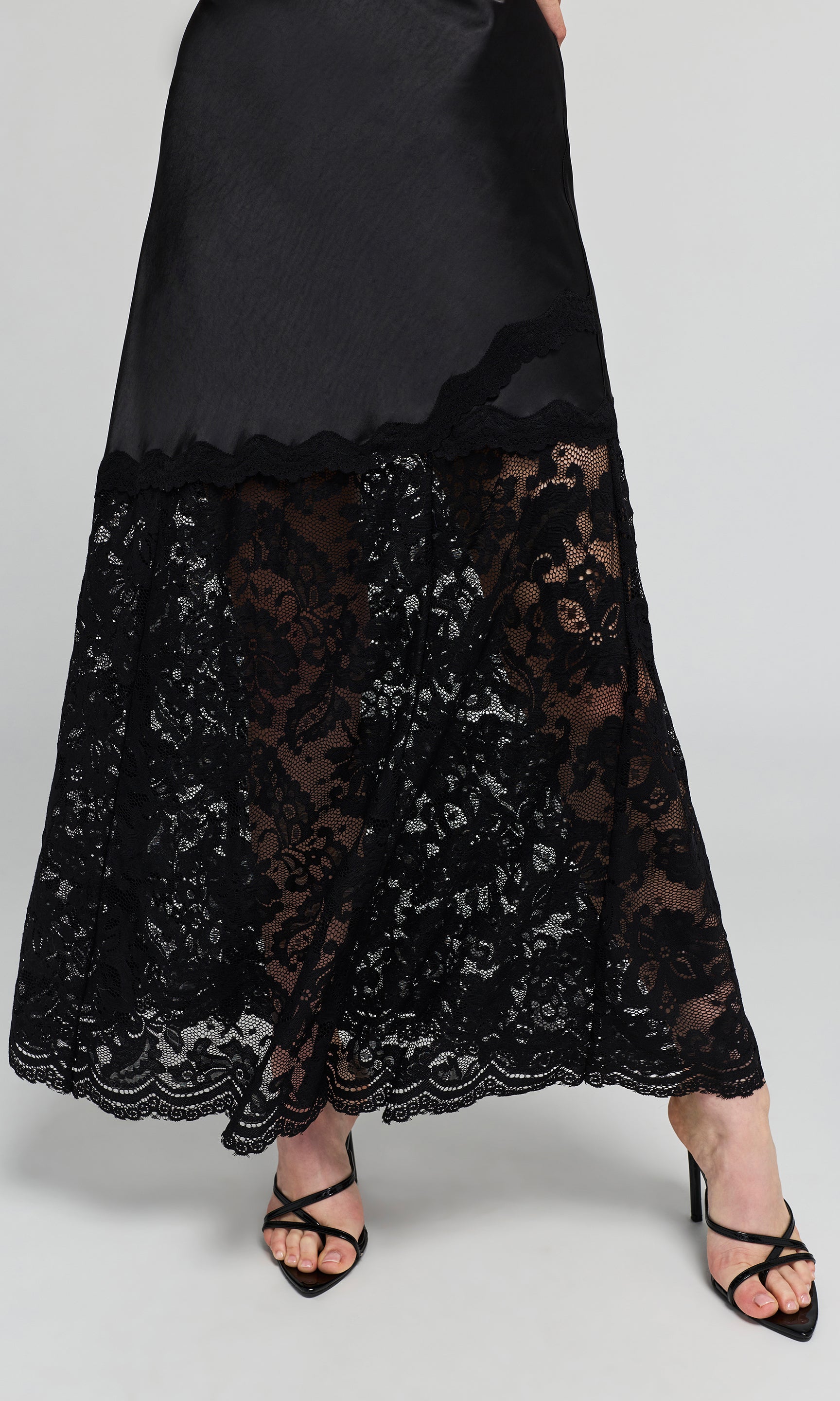 Close-up of midi skirt featuring a smooth satin-like upper section and a sheer floral lace lower section.
