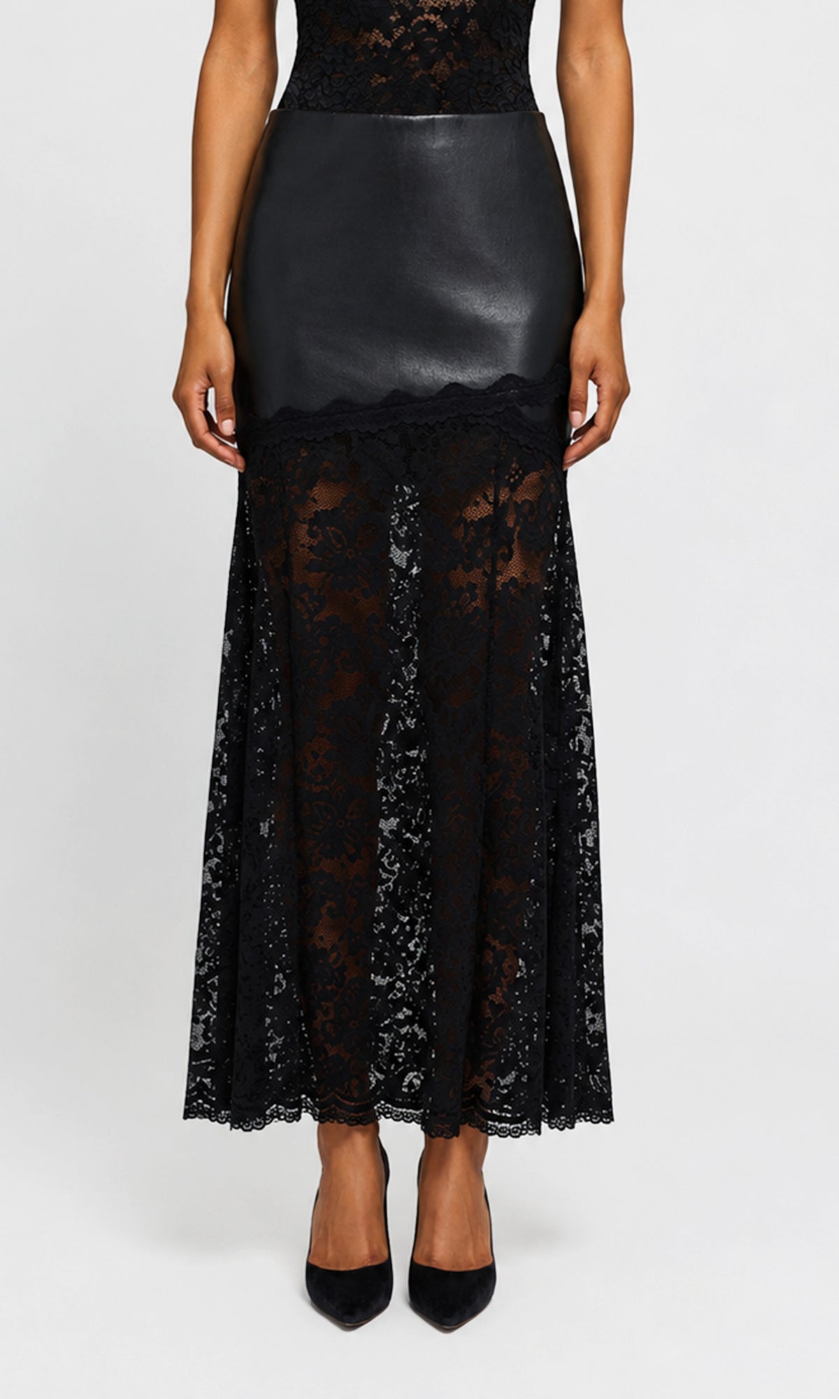 Model wearing a black midi skirt featuring a smooth faux-leather upper section and a sheer black lace lower skirt.