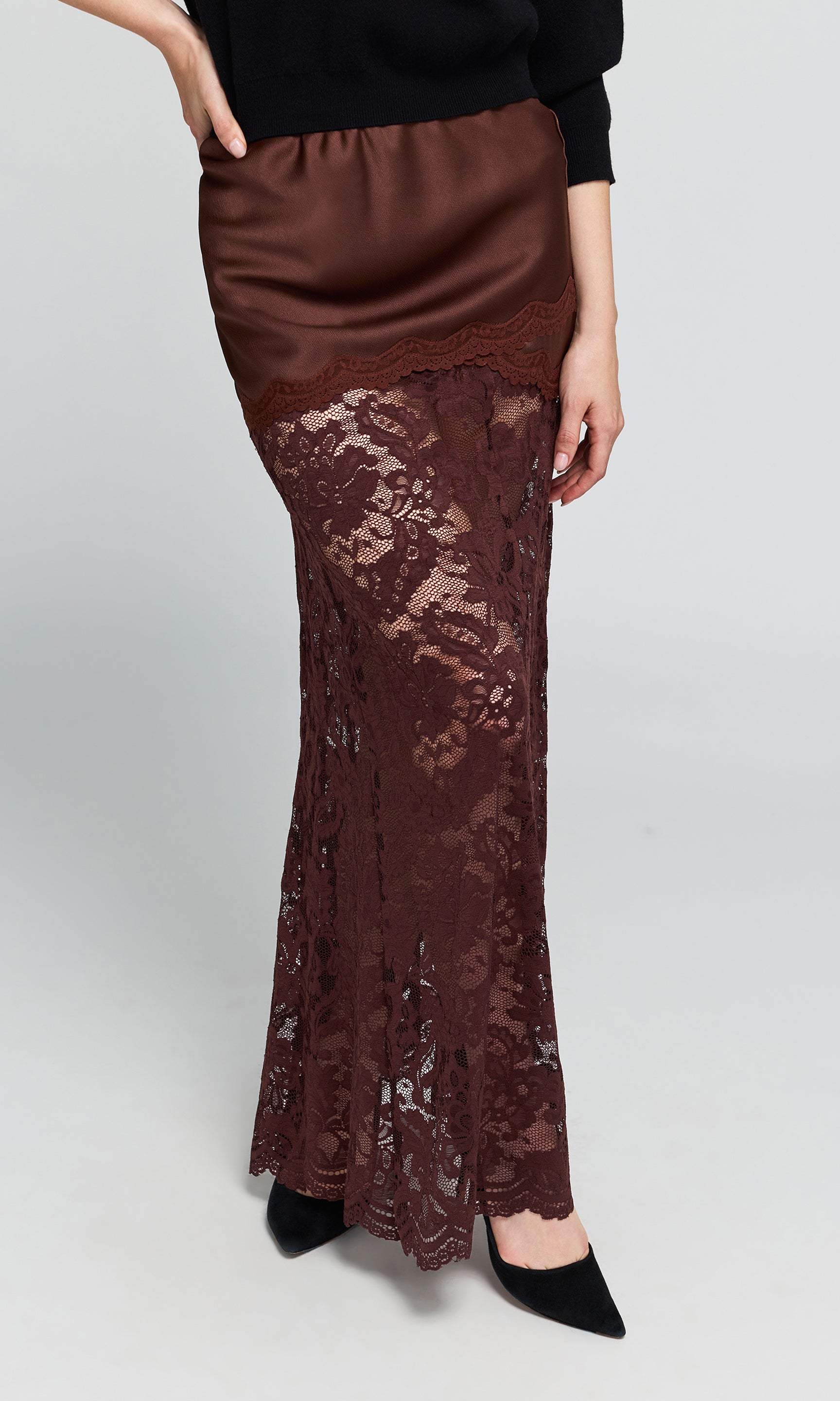 Side view of model wearing a brown lace maxi skirt with a sheer satin-like fabric, worn by a model with a black top.
